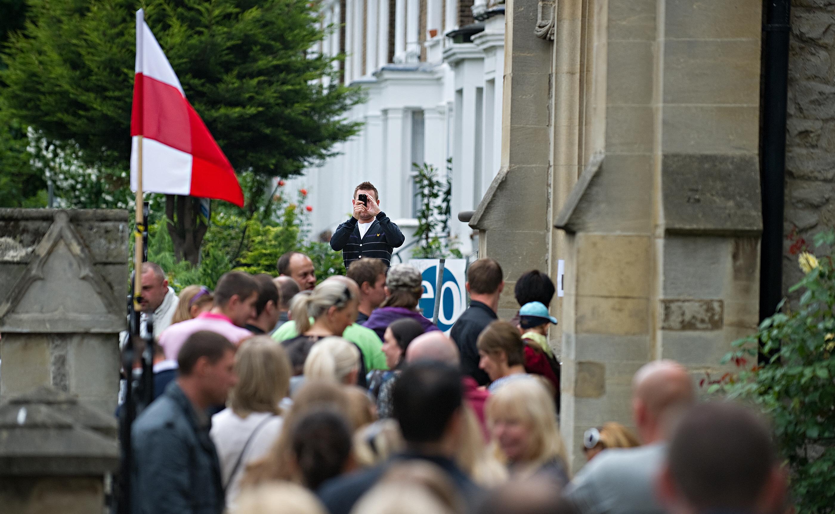 Ludzie tłoczą się przed budynkiem z polską flagą