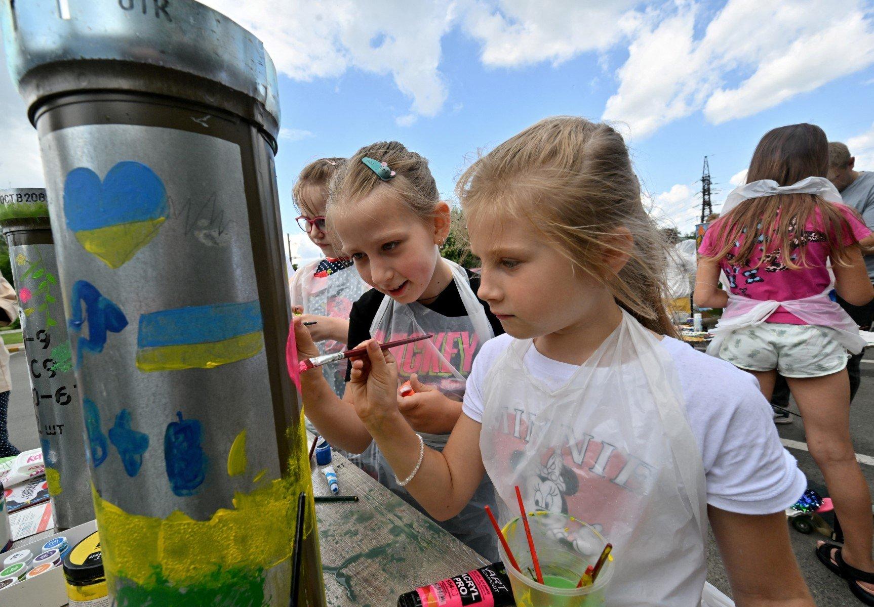 Dziewczynki malują ukraińskie symbole: żółto-niebieskie serca i flagi na dużej łusce po naboju postawionej pionowo.