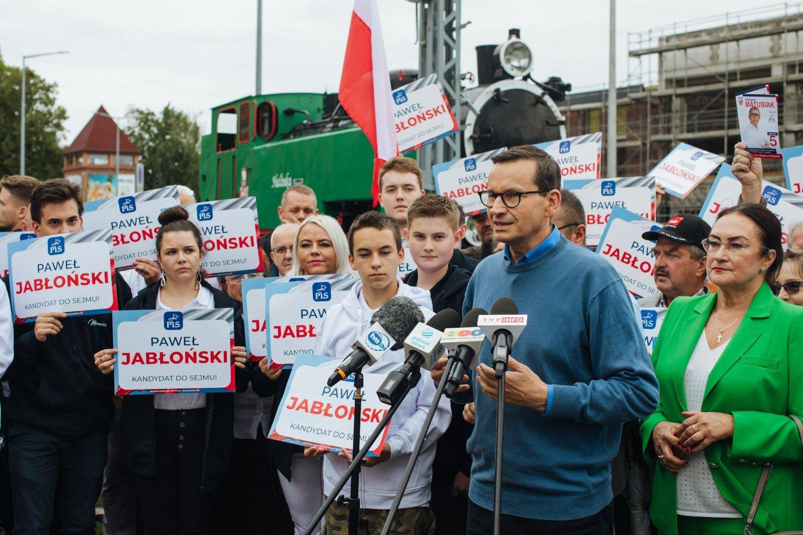 Morawiecki w niebieskim swetrze przemiawia do mikrofonu, w tle tłum działaczy pis
