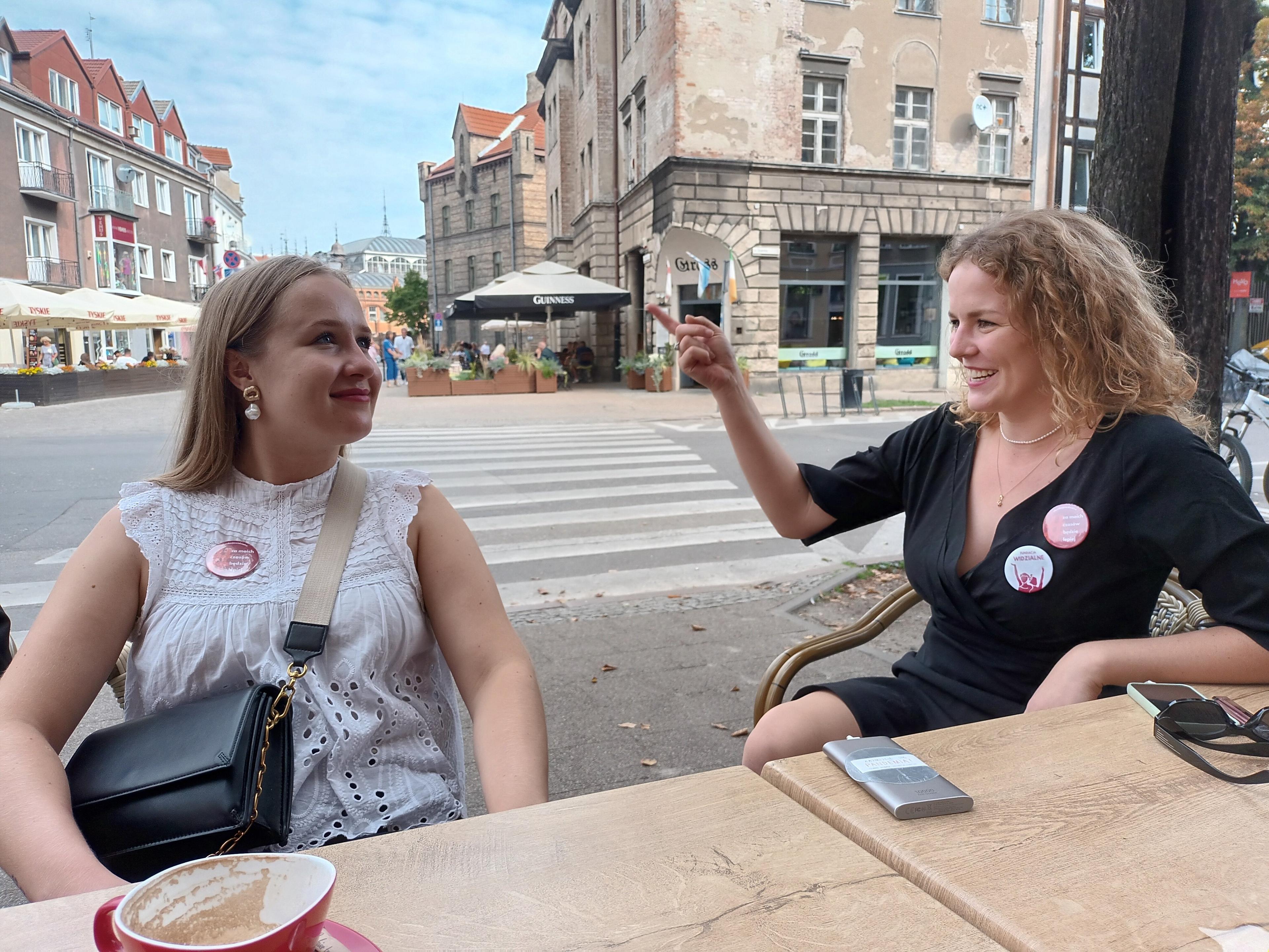 Dwie mlode kobiety rozmawiają przy stoliku na ulicy