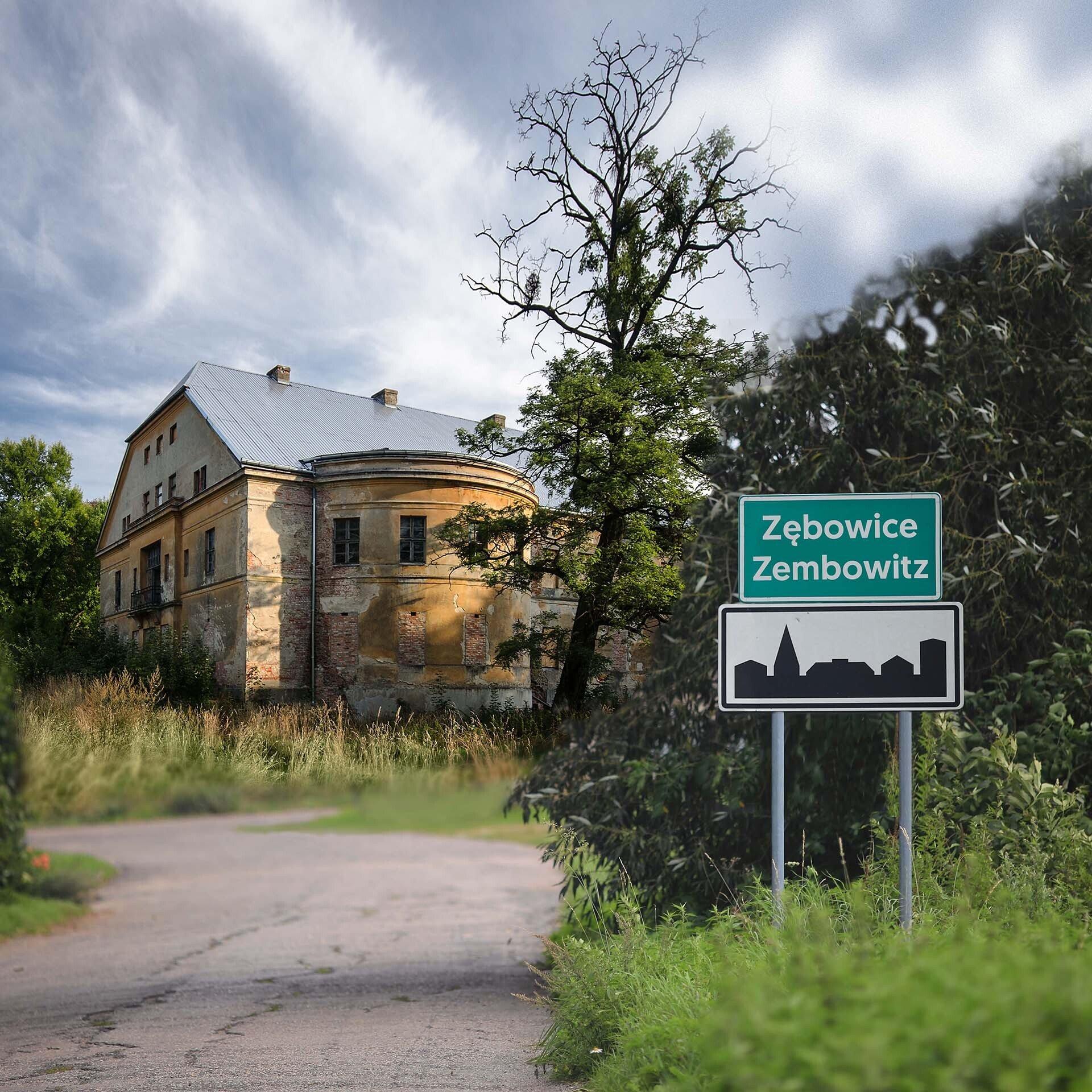 Zielona tablica z podwójną nazwą miejscowości: Zębowice i Zembowitz, w tle niszczejący pałac wśród zieleni.