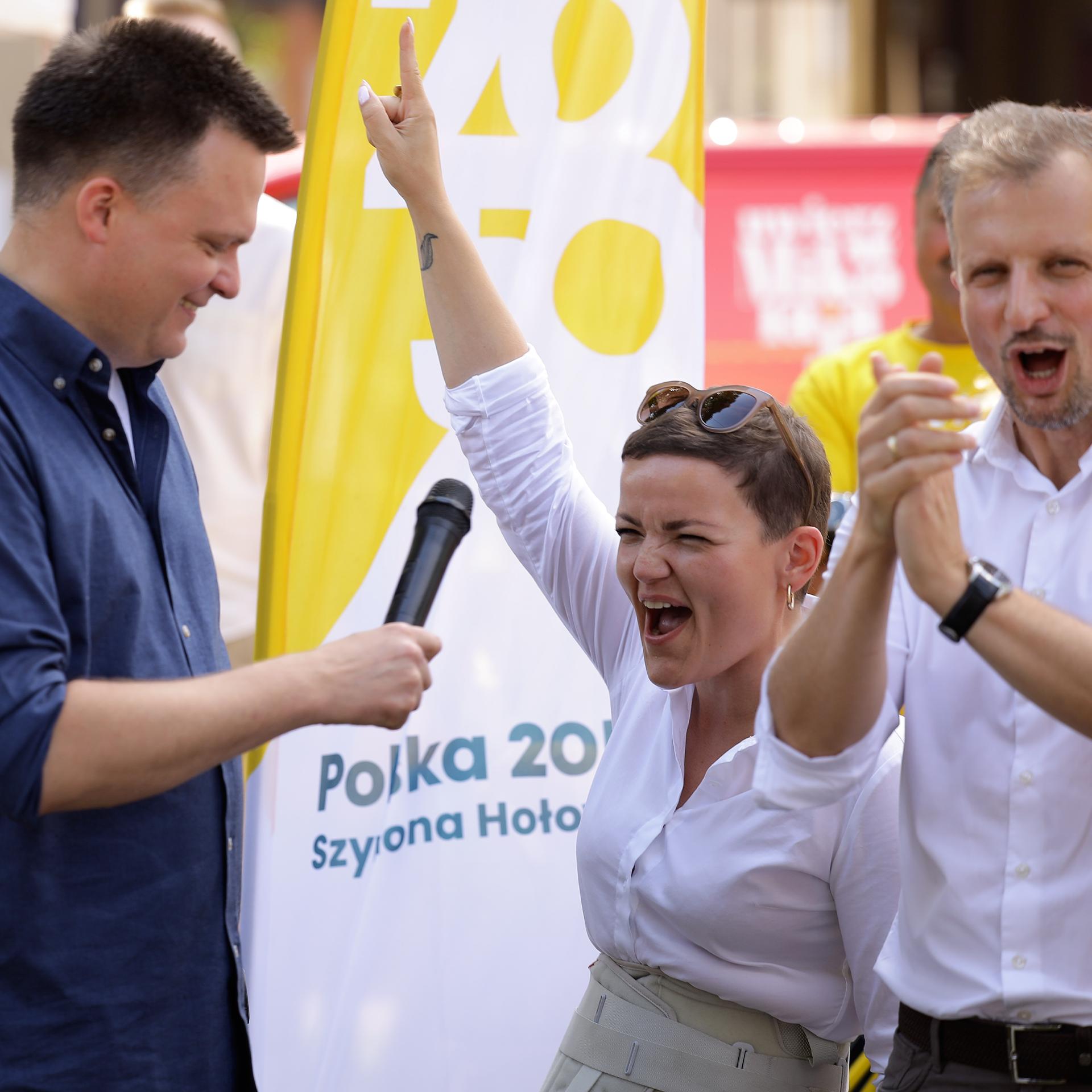 Marta Cienkowska podnosi rękę i radośnie krzyczy, obok stoi Szymon Hołownia z mikrofonem
