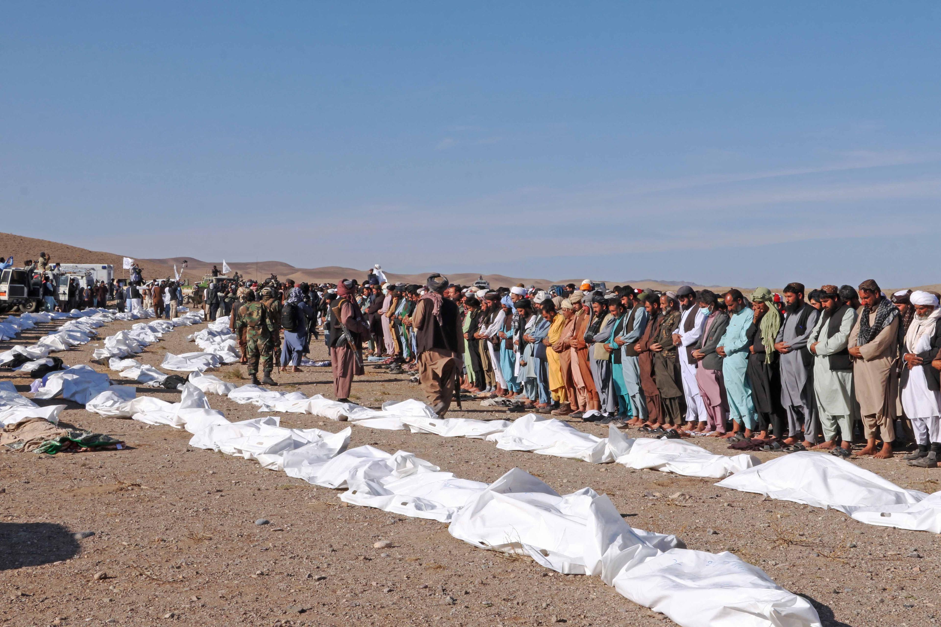 Afgańczycy stoją rzędem wzdłuż ułożonych na ziemi ciał ofiar trzęsienia ziemi, przykrytych białym płótnem.