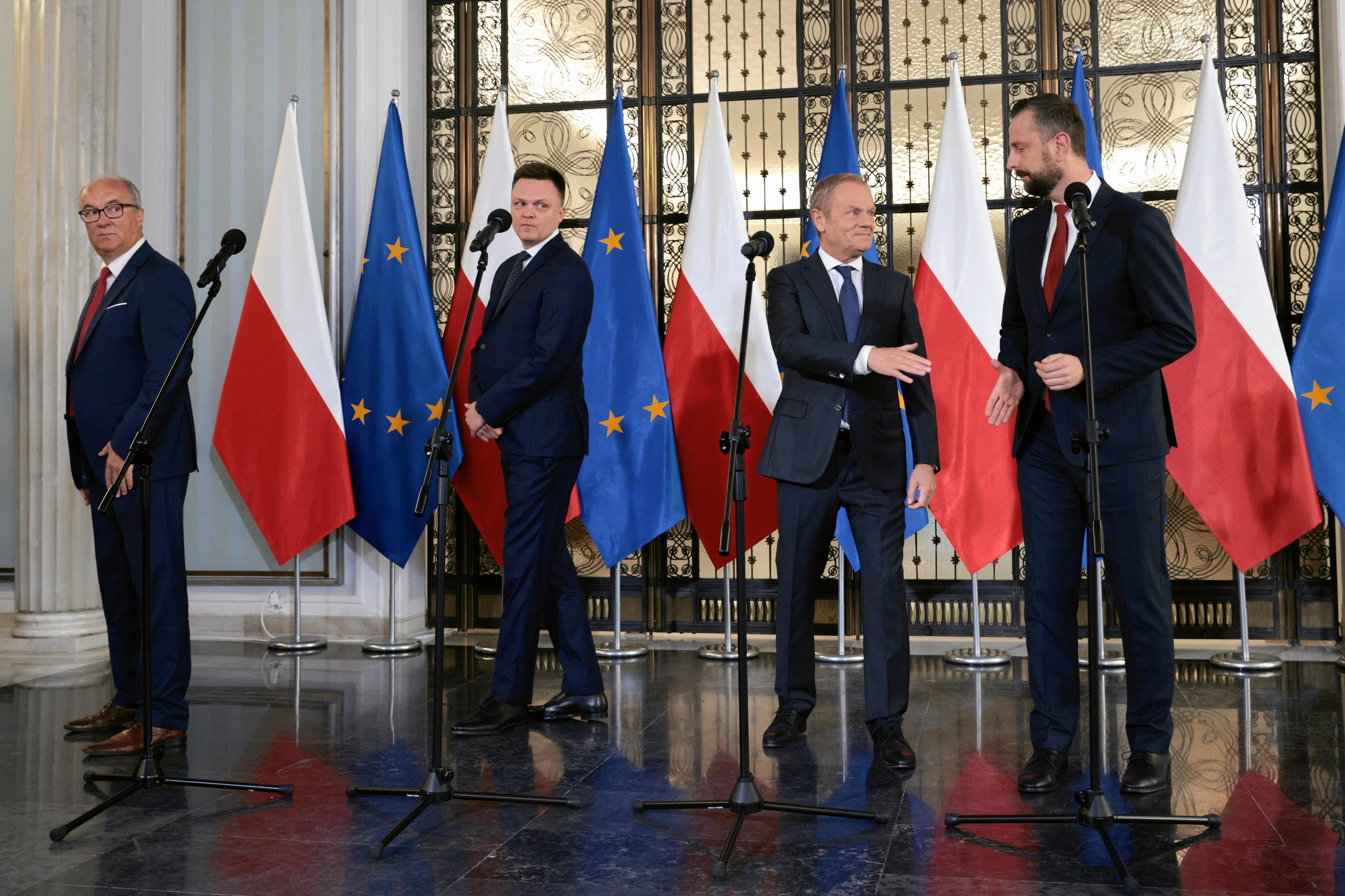 Czterech mężczyzn (od lewej: Czarzasty, Hołownia, Tusk, Kosiniak-Kamysz) stoi przed mikrofonami, ale każdy patrzy w inną stronę