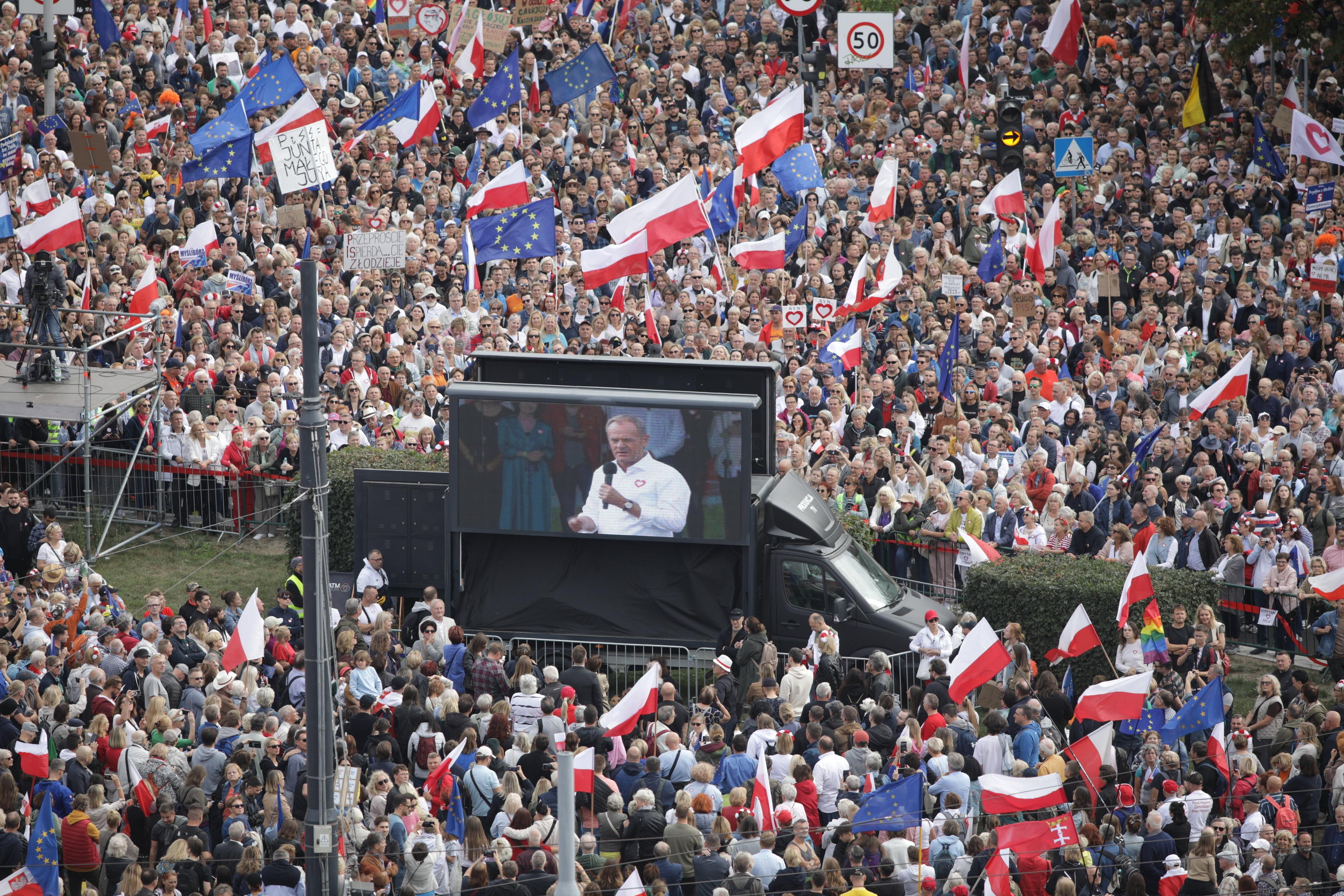 tłum ludzi z biało-czerwonymi flagami, na środku telebim, a na nim Donald Tusk