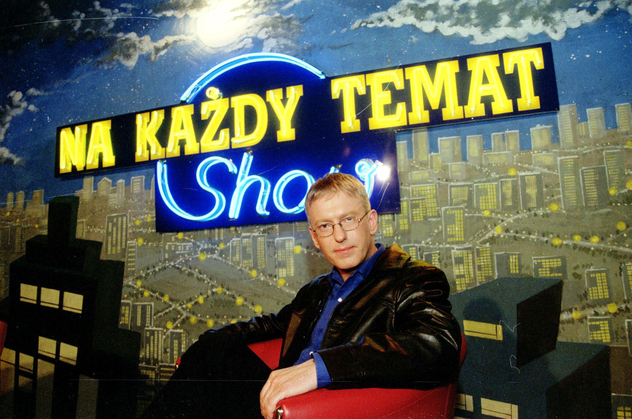 Mariusz Szczygieł w studiu programu „Na każdy temat”, siedzi w fotelu, w tle widać grafikę przedstawiającą panoramę miasta i napis Na każdy temat. Show.