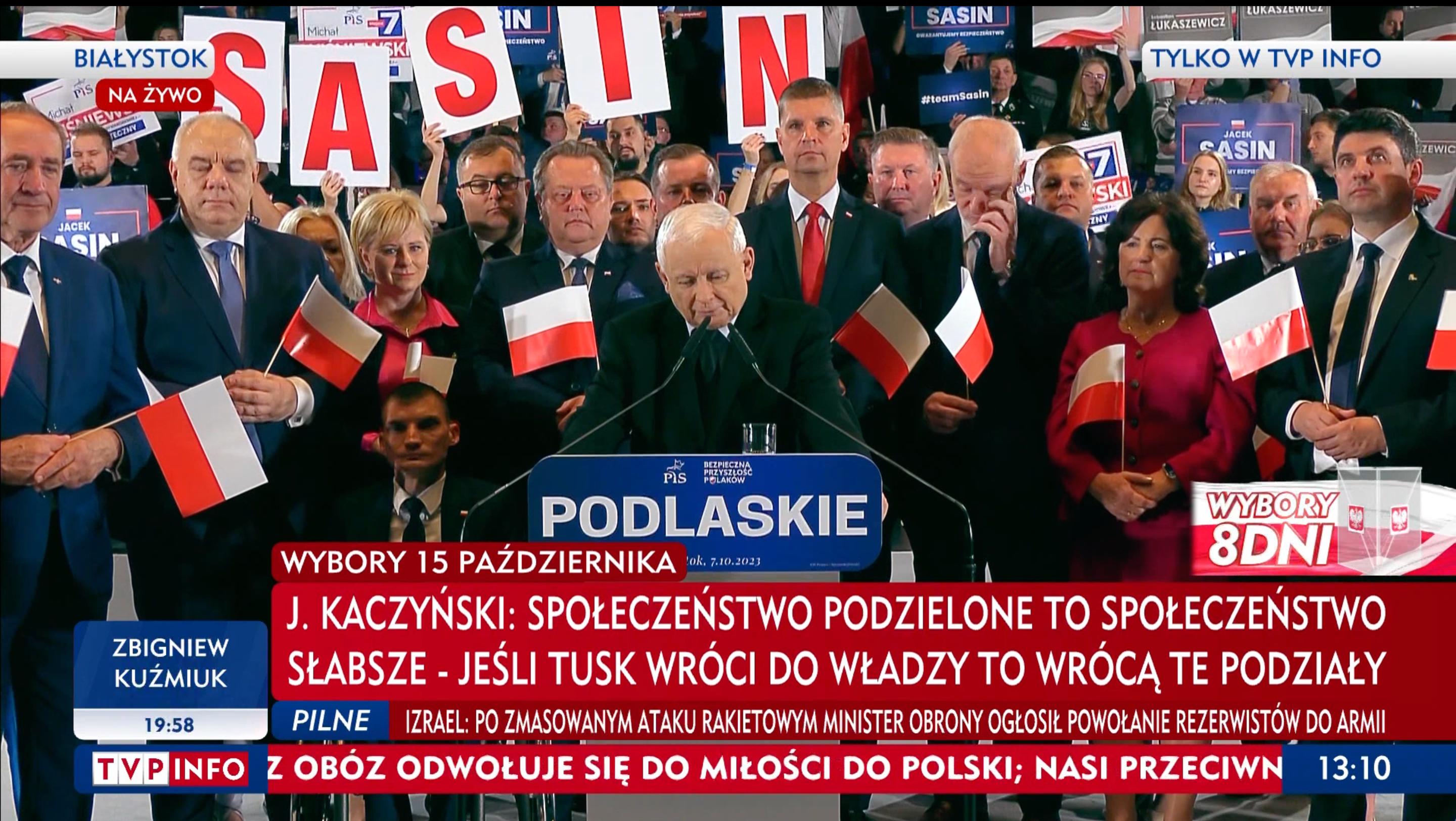 Kaczyński przemawia z mównicy w otoczeniu działaczy PiS