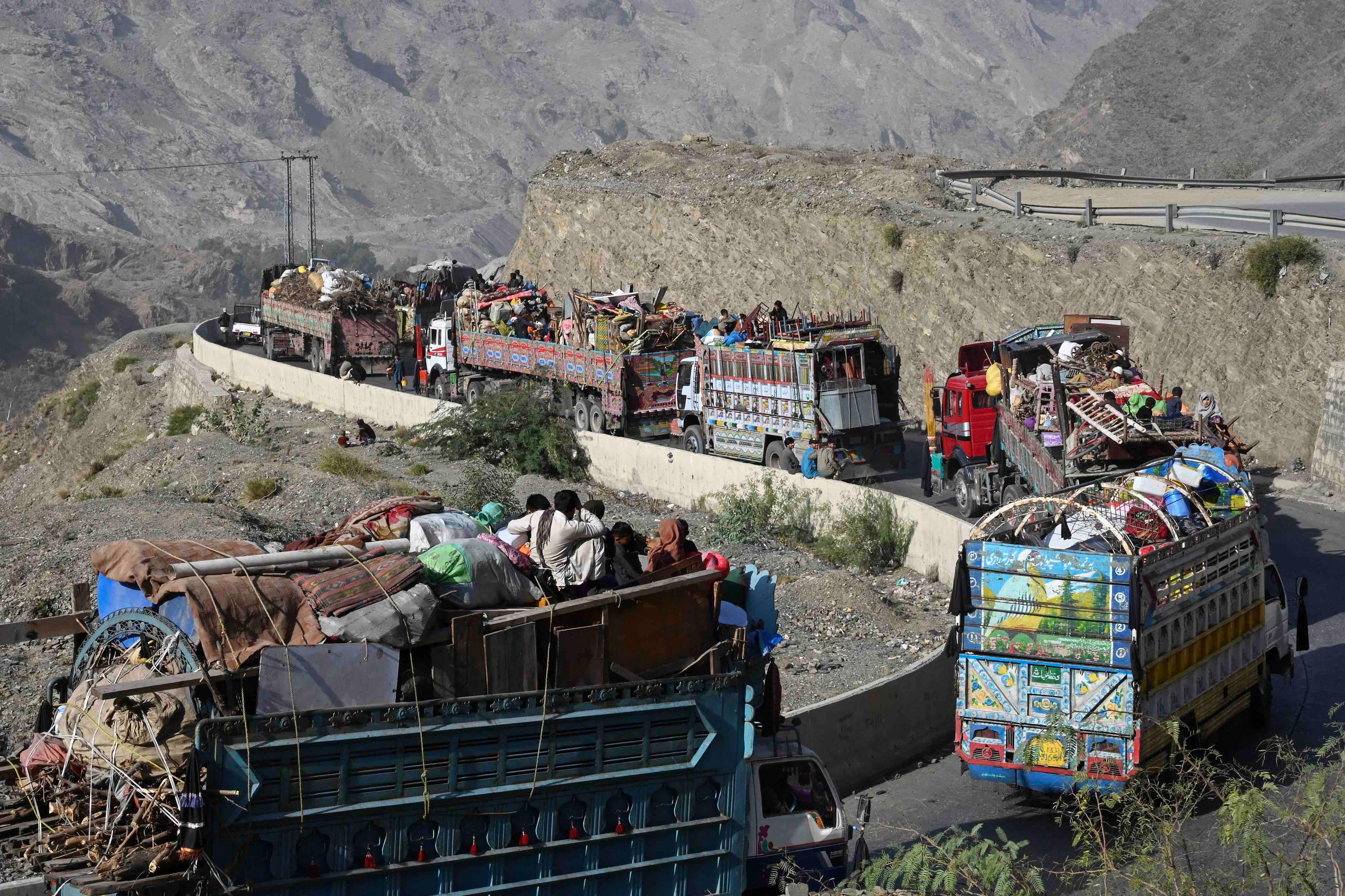 Sznur ciężarówek załadowanych rzeczami afgańskich uchodźców jedzie krętą drogą przez góry.