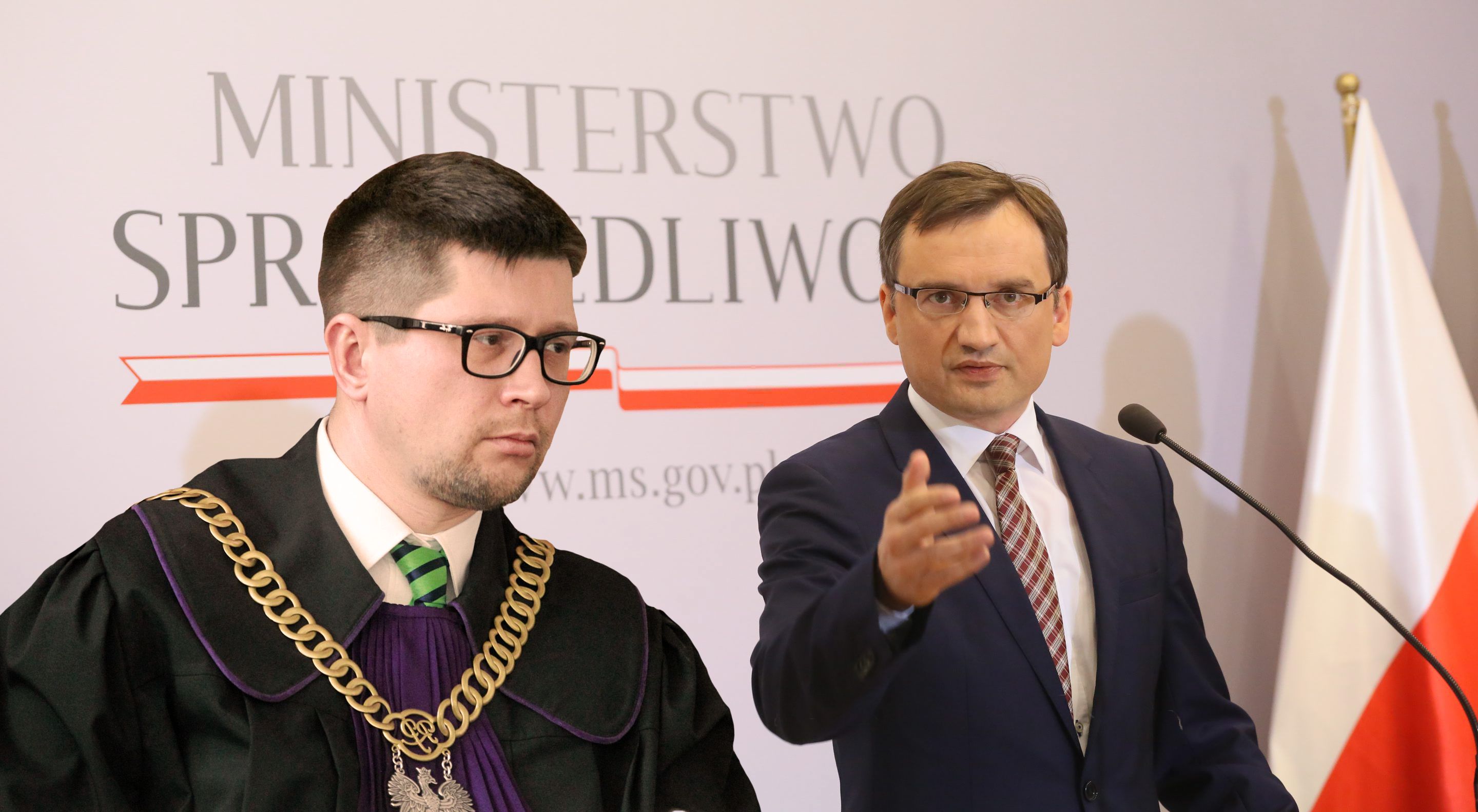 Mężczyzna w okularach i todze obok mężczyzny w garniturze