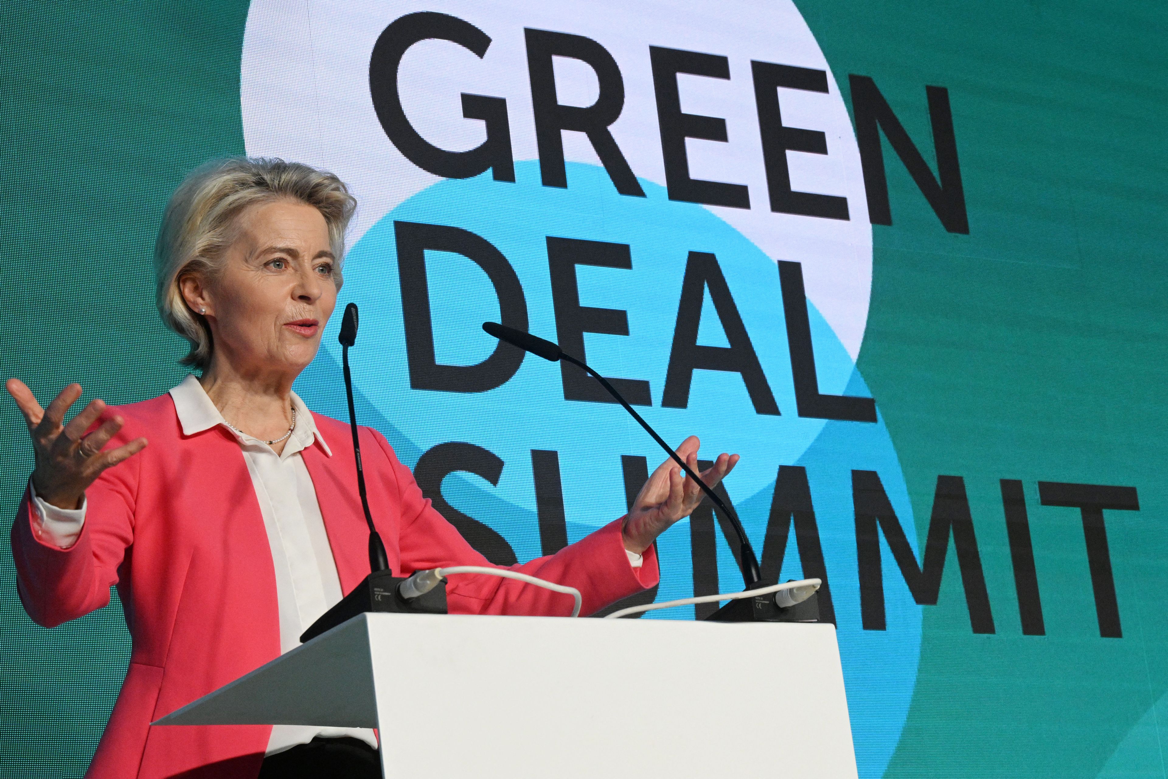 Ursula von der Leyen w czerwonej marynarce na zielonym tle, za nią napis green deal summit