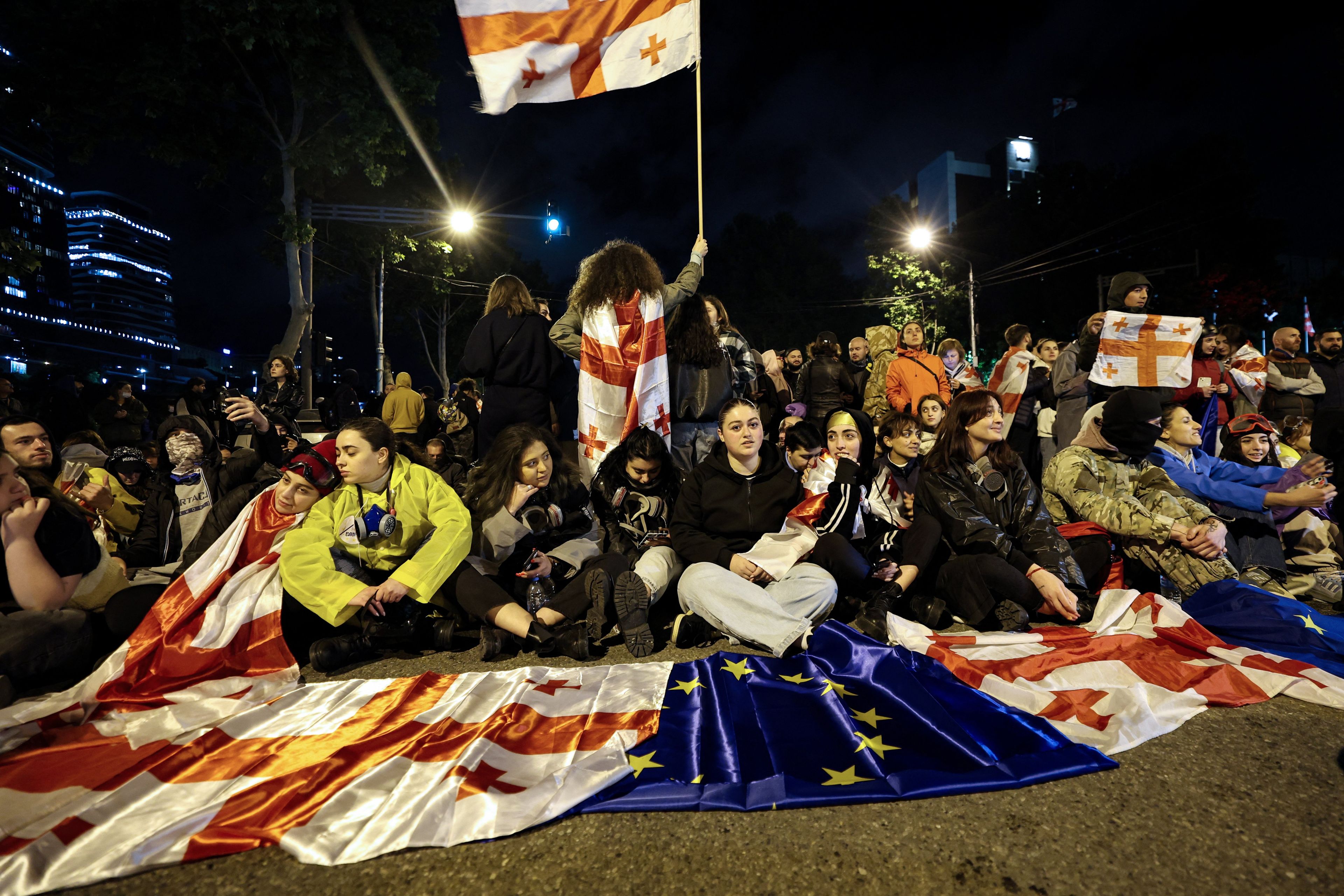 Młodzi ludzie siedza na jezdni z flagami Gruzji i UE