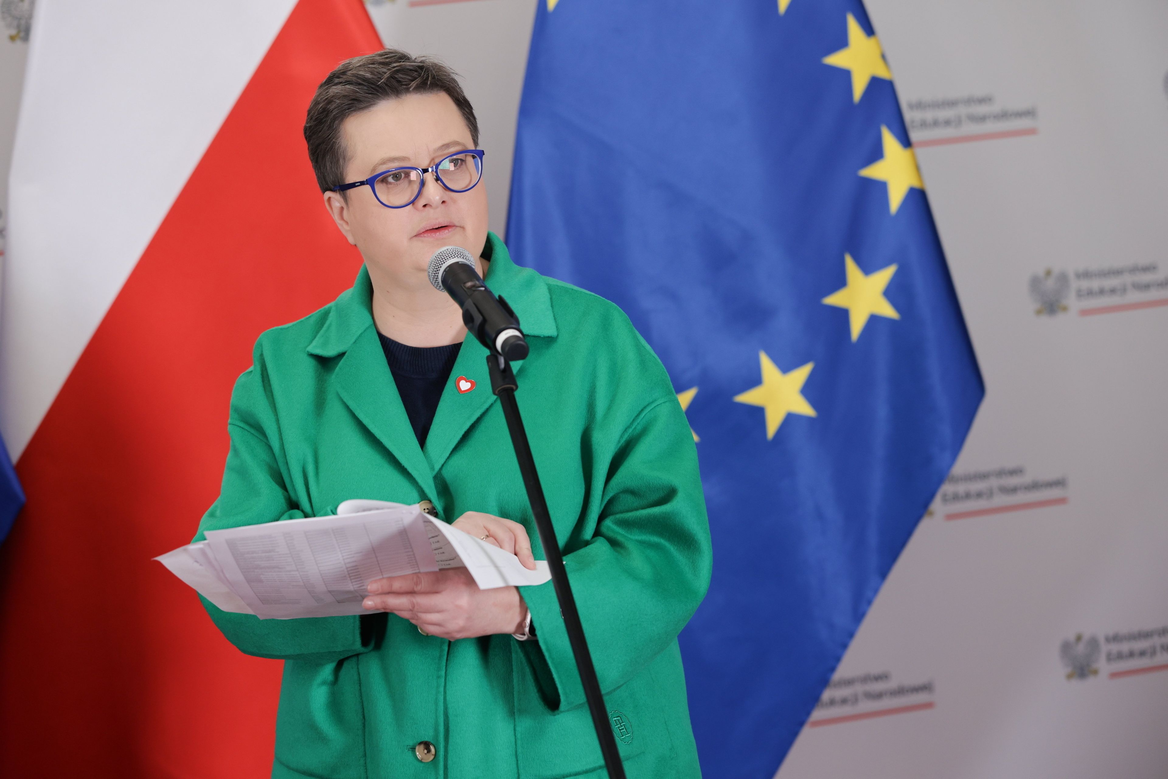 Kobieta w zielonym żakiecie z plikiem papierów w ręku