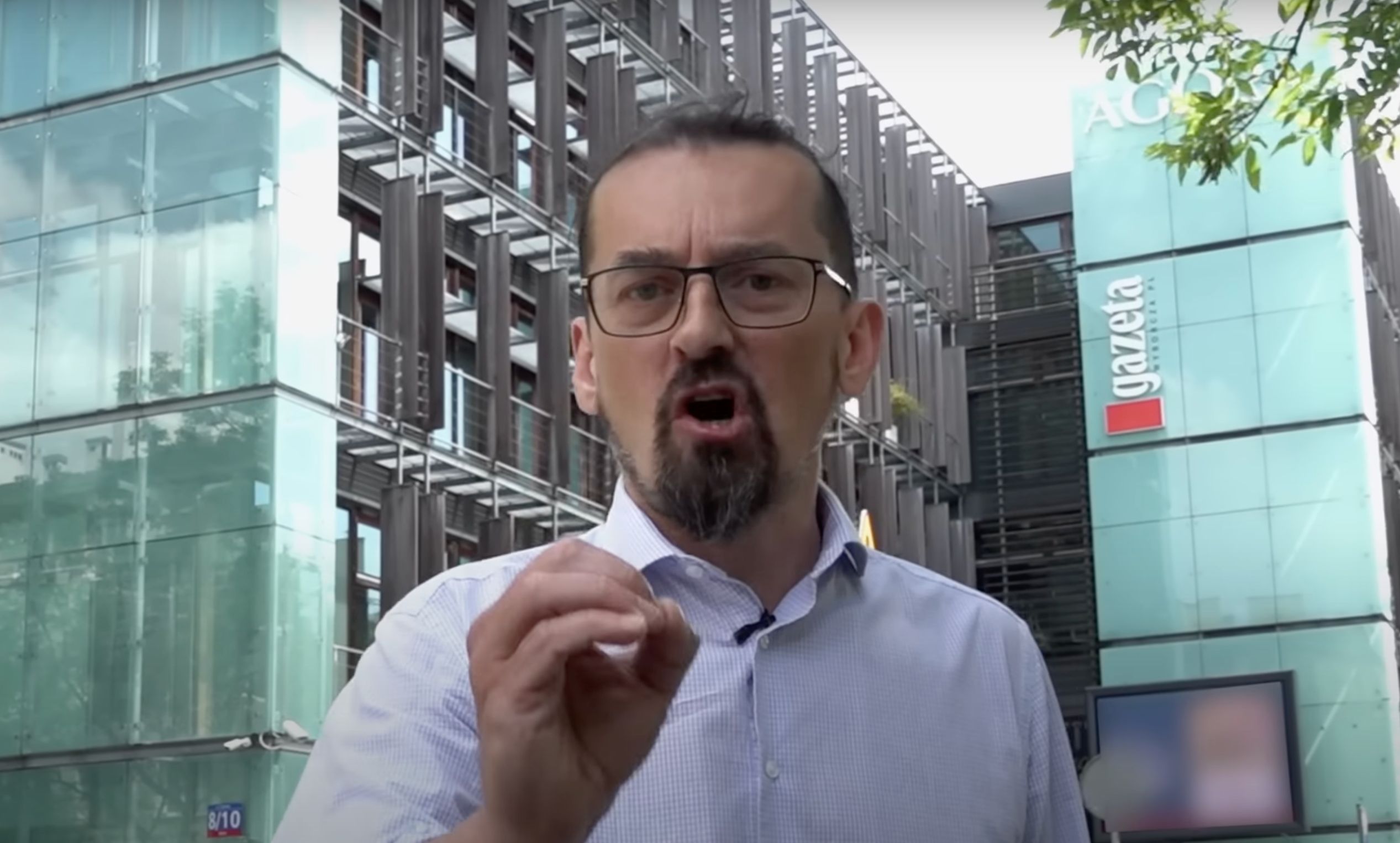 Mariusz Zielke przemawia do kamery na tle budynku Agory z logo "Gazety Wyborczej". Kadr z filmu "Bagno".