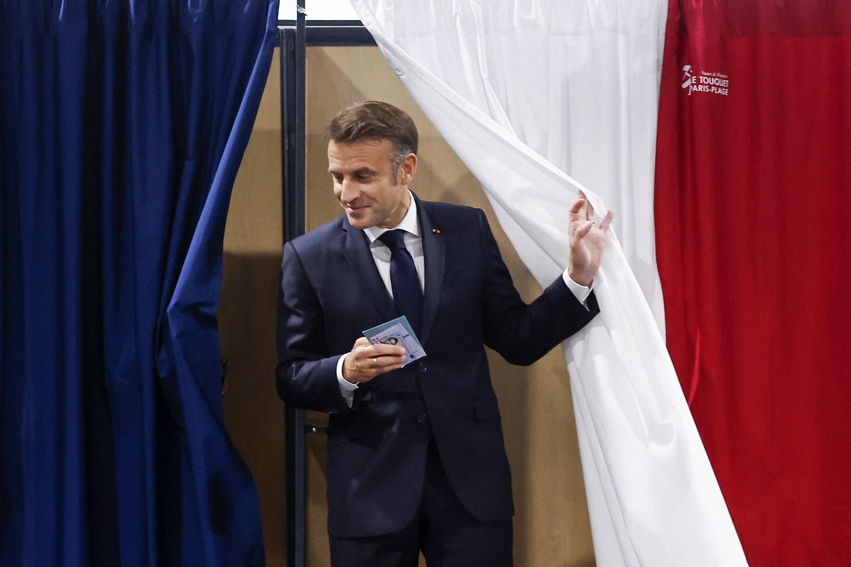 France's President Emmanuel Macron exits a polling booth, adorned with curtains displaying the colors of the flag of France, to vote in the second round of France's legislative election at a polling station in Le Touquet, northern France on July 7, 2024. France votes in legislative elections on July 7, 2024 that will be decisive in determining its political future and could see the far right become the largest party in parliament for the first time. (Photo by MOHAMMED BADRA / POOL / AFP)