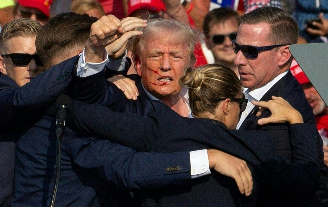 Donald Trump na wiecu, tu po zamachu, podnosi w górę pięść w otoczeniu ochroniarzy