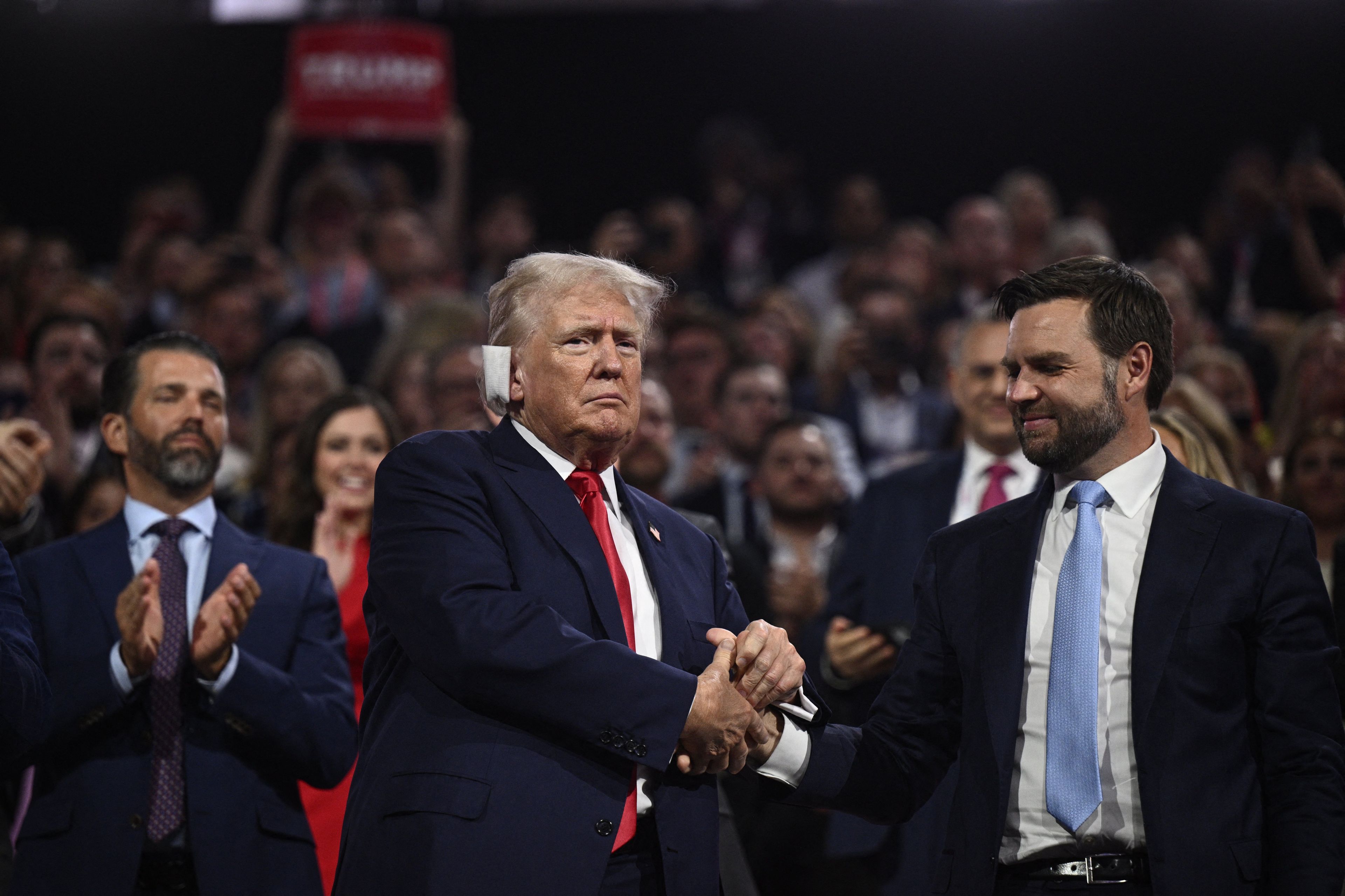Dwóch mężczyzn (Donald Trump i James David Vance) stoi obok siebie, ściskając sobie ręce, w tle publiczność