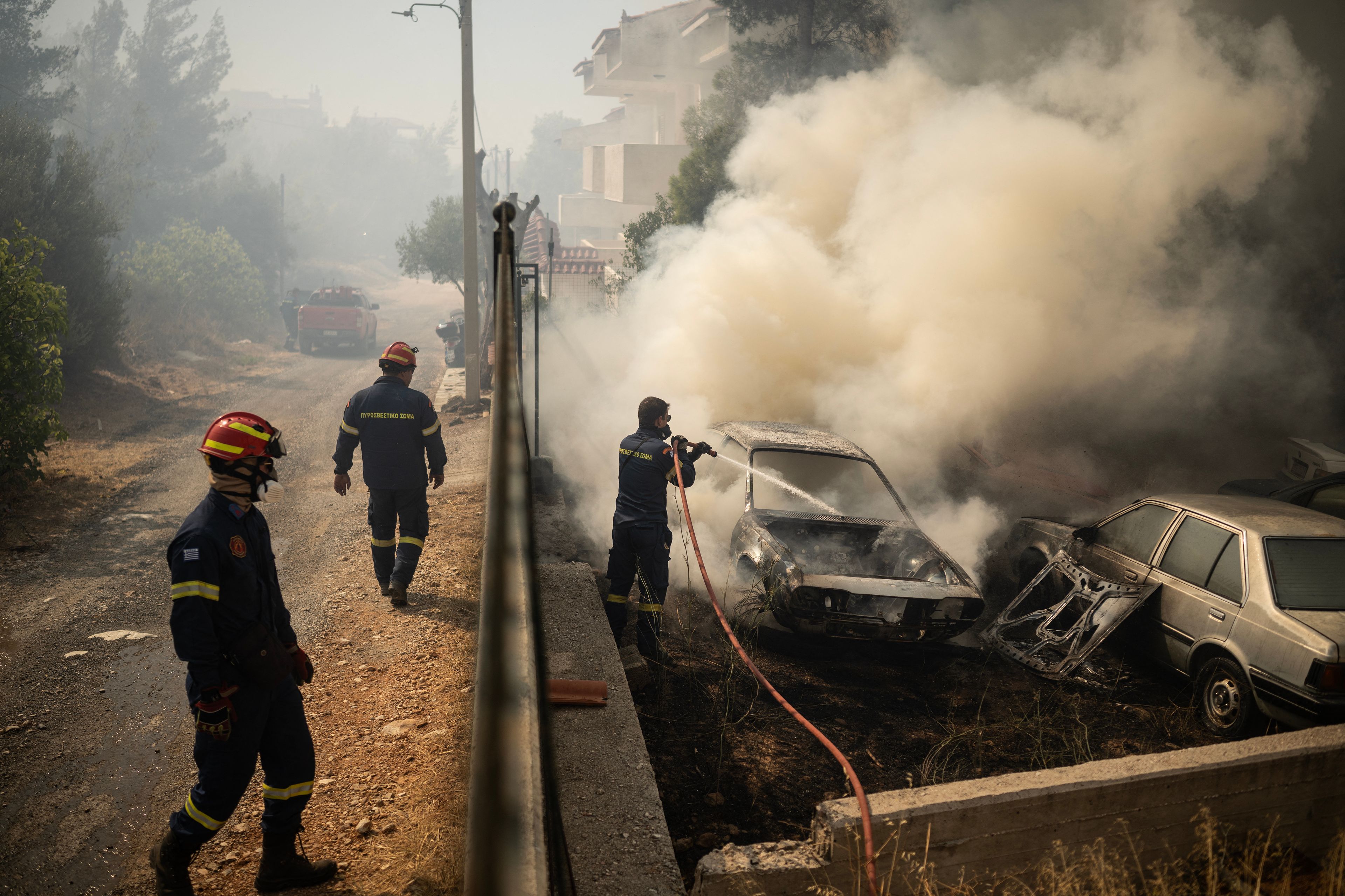 A firefighter sprays water to a burning car during a wildfire in Dione on August 12, 2024. - On August 12, 2024, Greece's civil protection authorities ordered the evacuation of several towns in the north-eastern suburbs of Athens, threatened by a violent fire that started the day before and is spreading. (Photo by Angelos TZORTZINIS / AFP)
