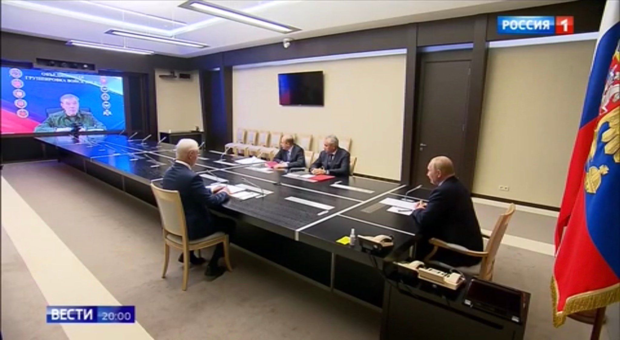 Putin, minister obrony, szef FSB i Szojgu (czterej męzczyźni w garniturach) siedzą przy długim stole i patrzą w ekran, na którym widać wojskowego (Gierasimowa)