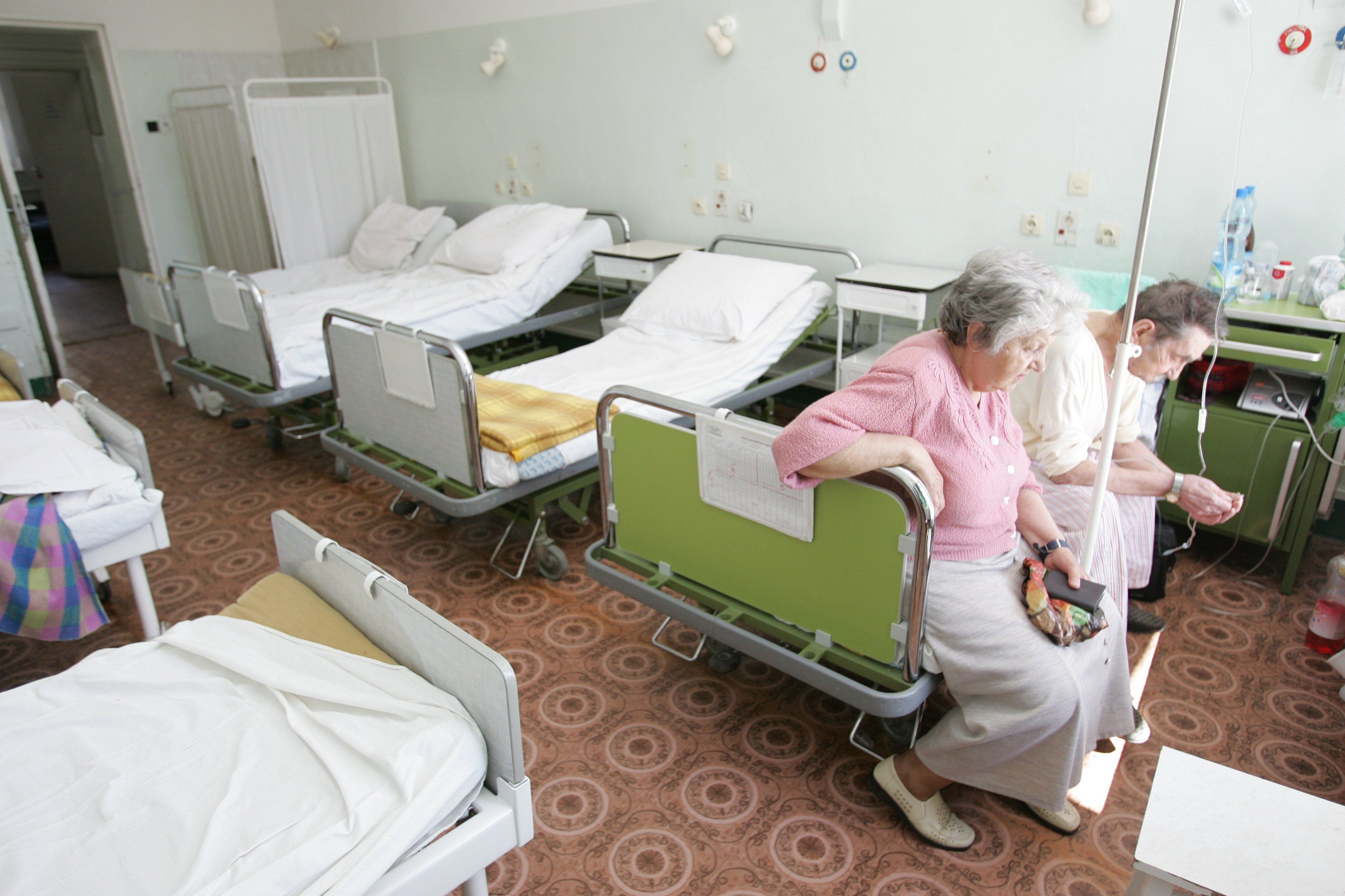 Pusta sala szpitalna. Dwie starsze kobiety siedzą na jednym łóżku