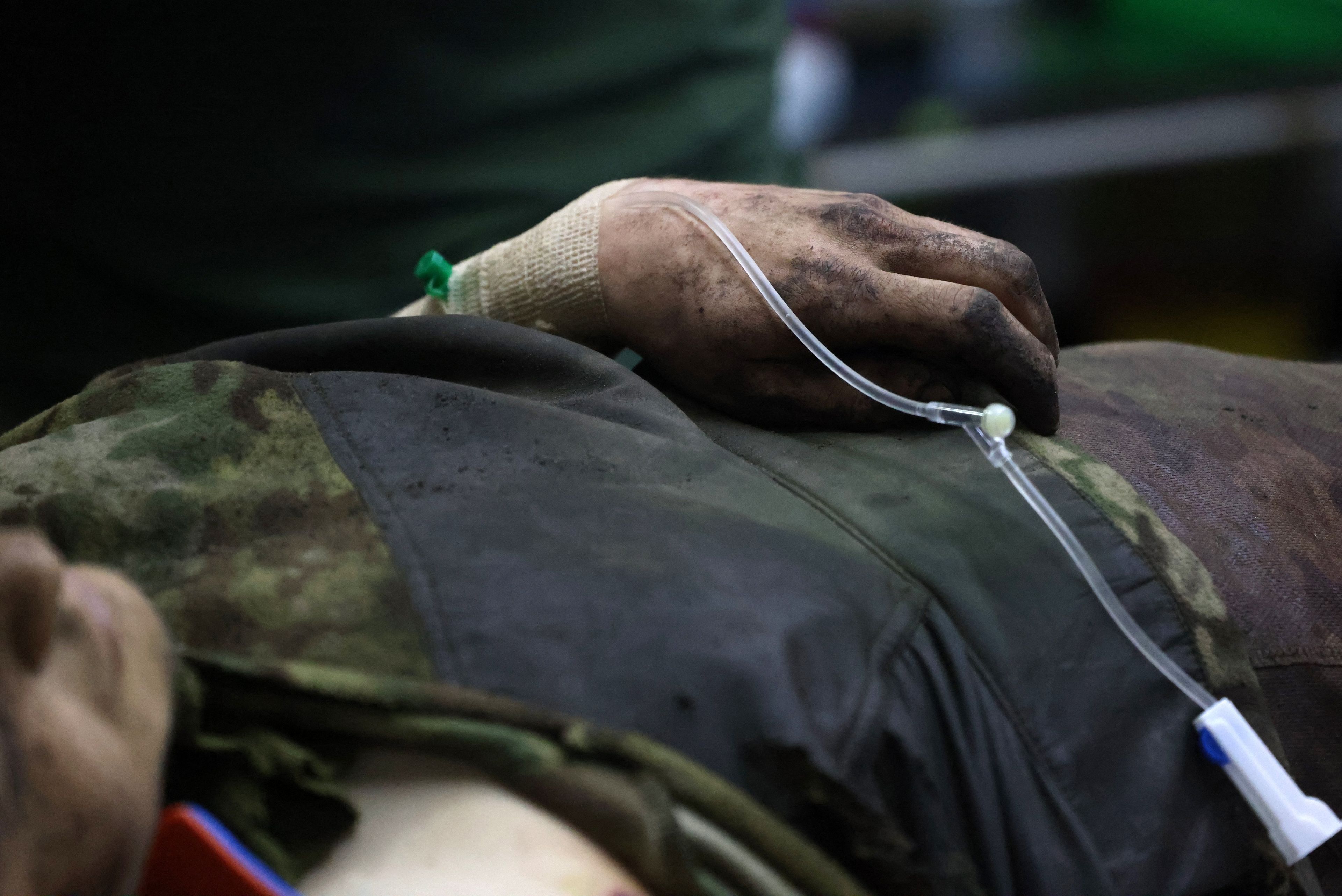 Na zdjęciu widać ludzki tułów i brudną rękę z króplówką. Odzież osoby też jest brudna, wiadać fragmenty kamuflażu