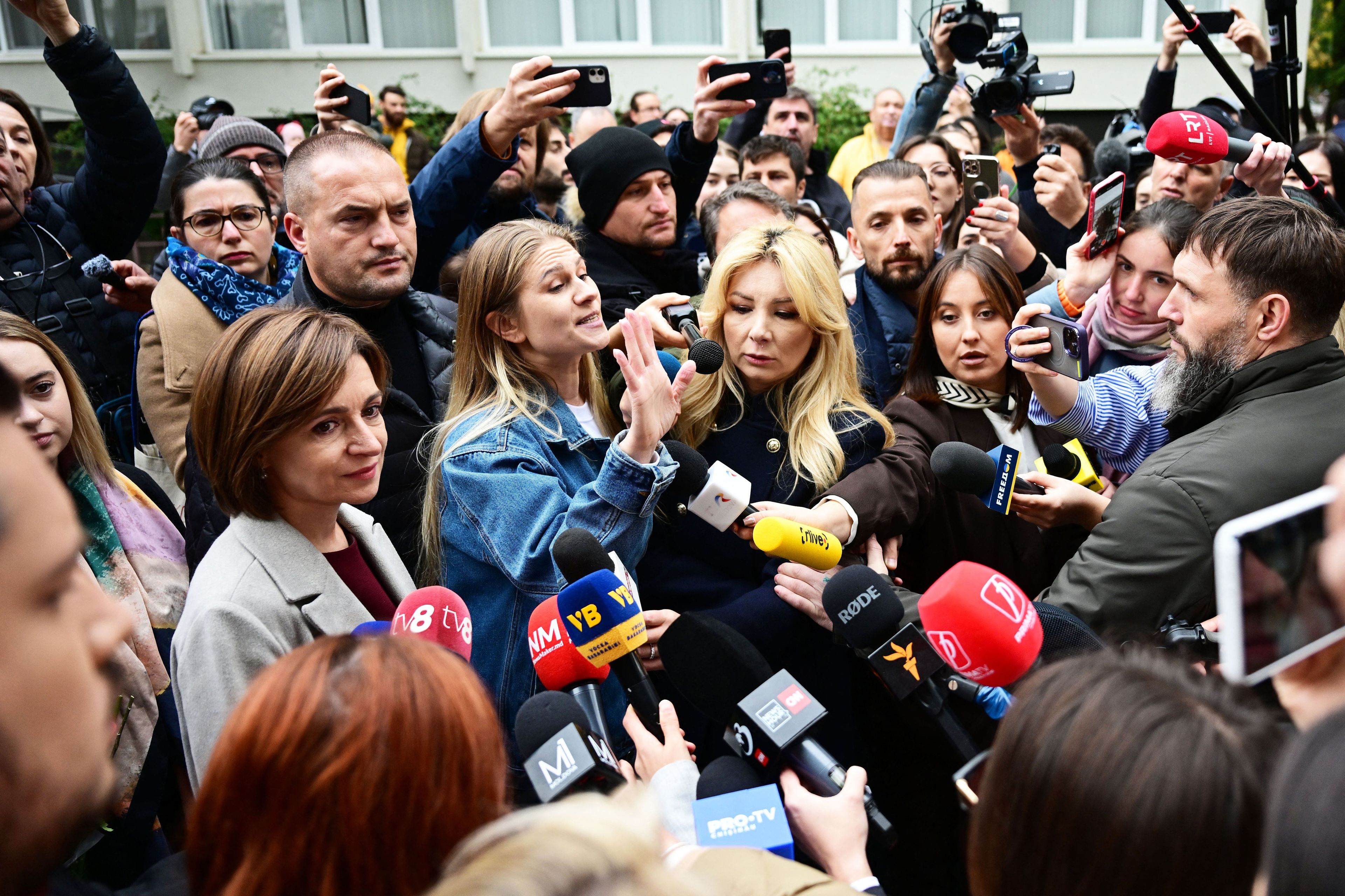 Kobieta w jasnym żakiecie wśród tłumu dziennikarzy