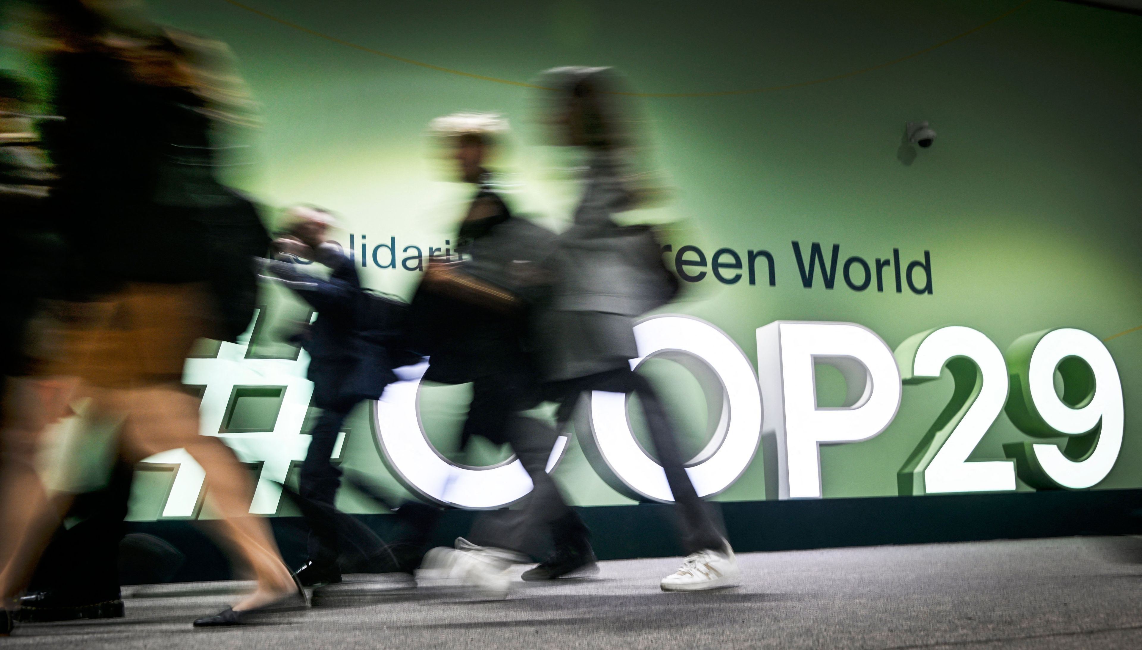 Zdjęcie przedstawia sylwetki osób na tle wielkiego napisu COP29