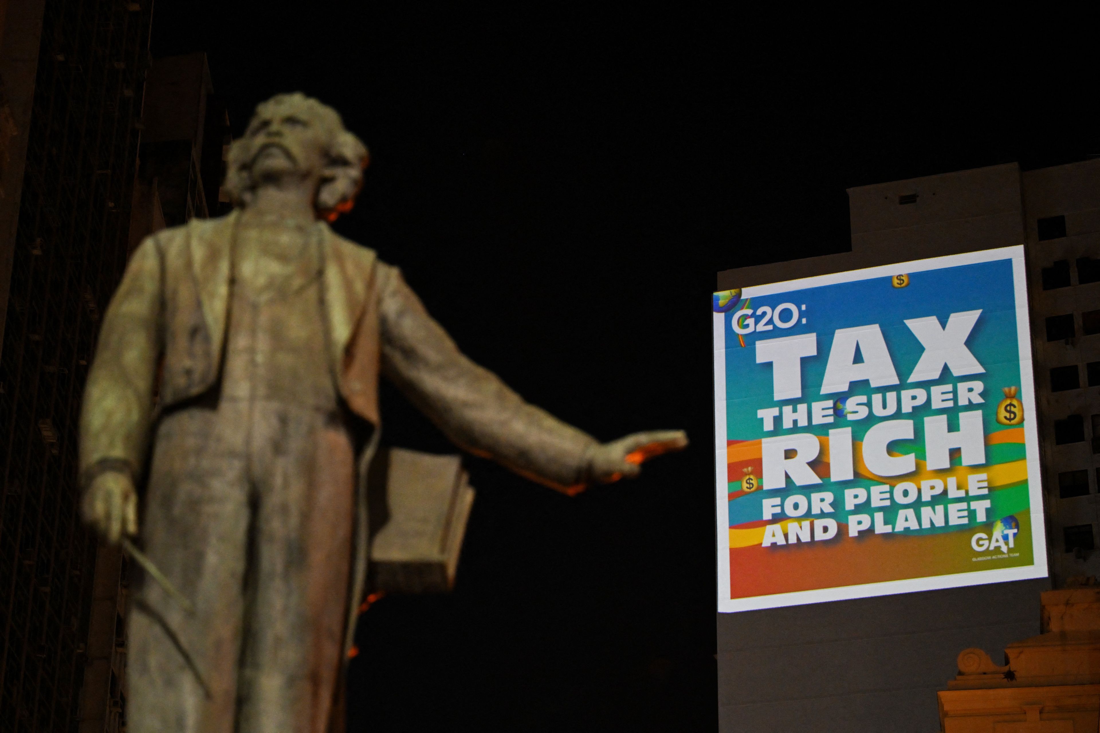 A group of environmental activists projects on a building slide with a silhouette depicting US president-elect Donald Trump that reads, "Tax the super rich for the people and planet" on November 18, 2024, in Rio de Janeiro, Brazil, during the G20 Summit. - ONG environment demonstrates projecting slides to demand governments to take actions and tax the superriches for the benefit of the planet. (Photo by LUIS ROBAYO / AFP)