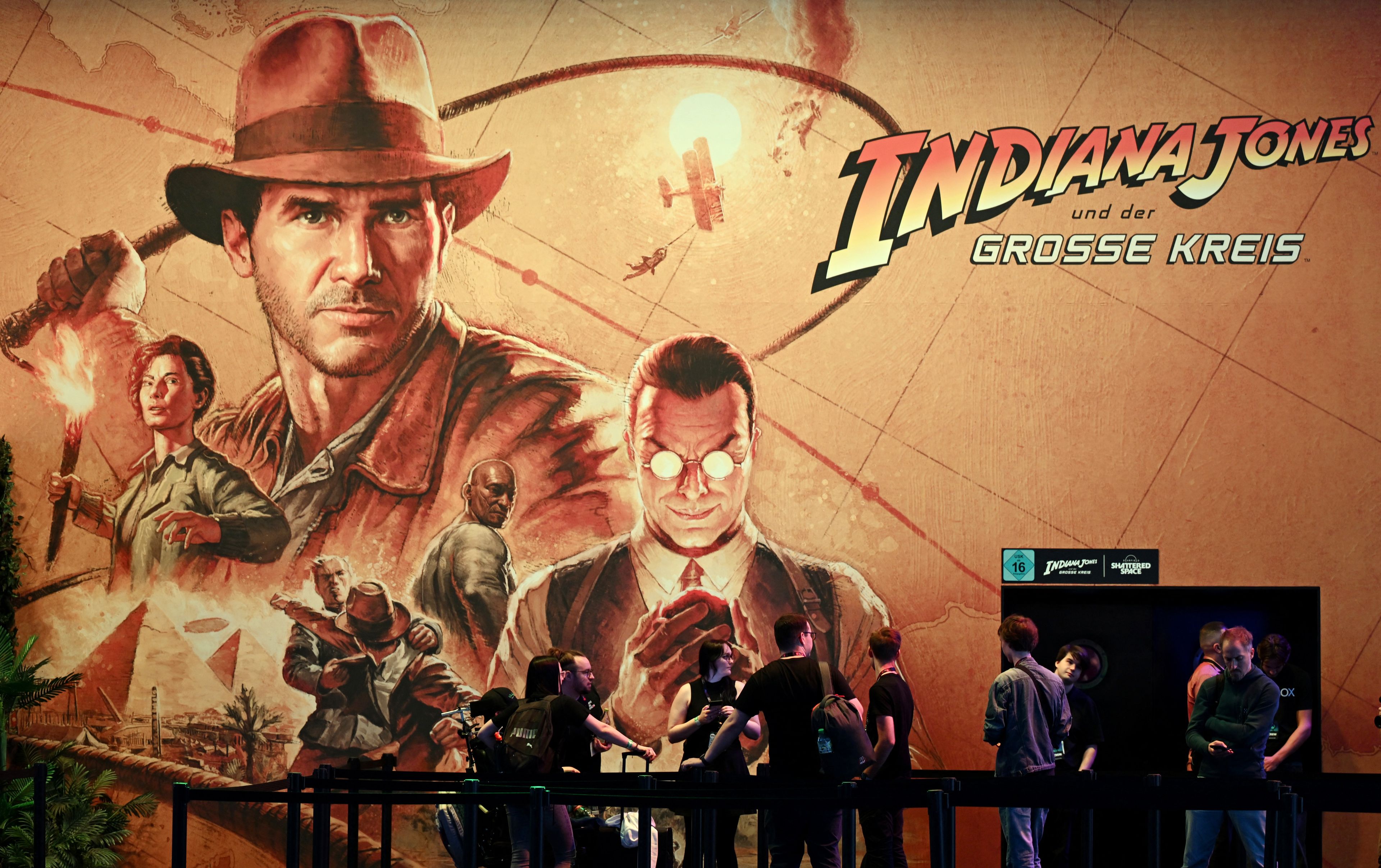 (FILES) Visitors stand at the booth of the video game 'Indiana Jones and the Great Circle' during the media day at the Gamescom video games trade fair in Cologne, western Germany on August 21, 2024. - The creators of the video game "Indiana Jones and the great circle", released on December 2, are thrusting players back to the time period of the first Indiana Jones film, "Raiders of the Lost Ark". Players get to inhabit the hero in the first person, in all his youthful splendour. (Photo by Ina FASSBENDER / AFP)