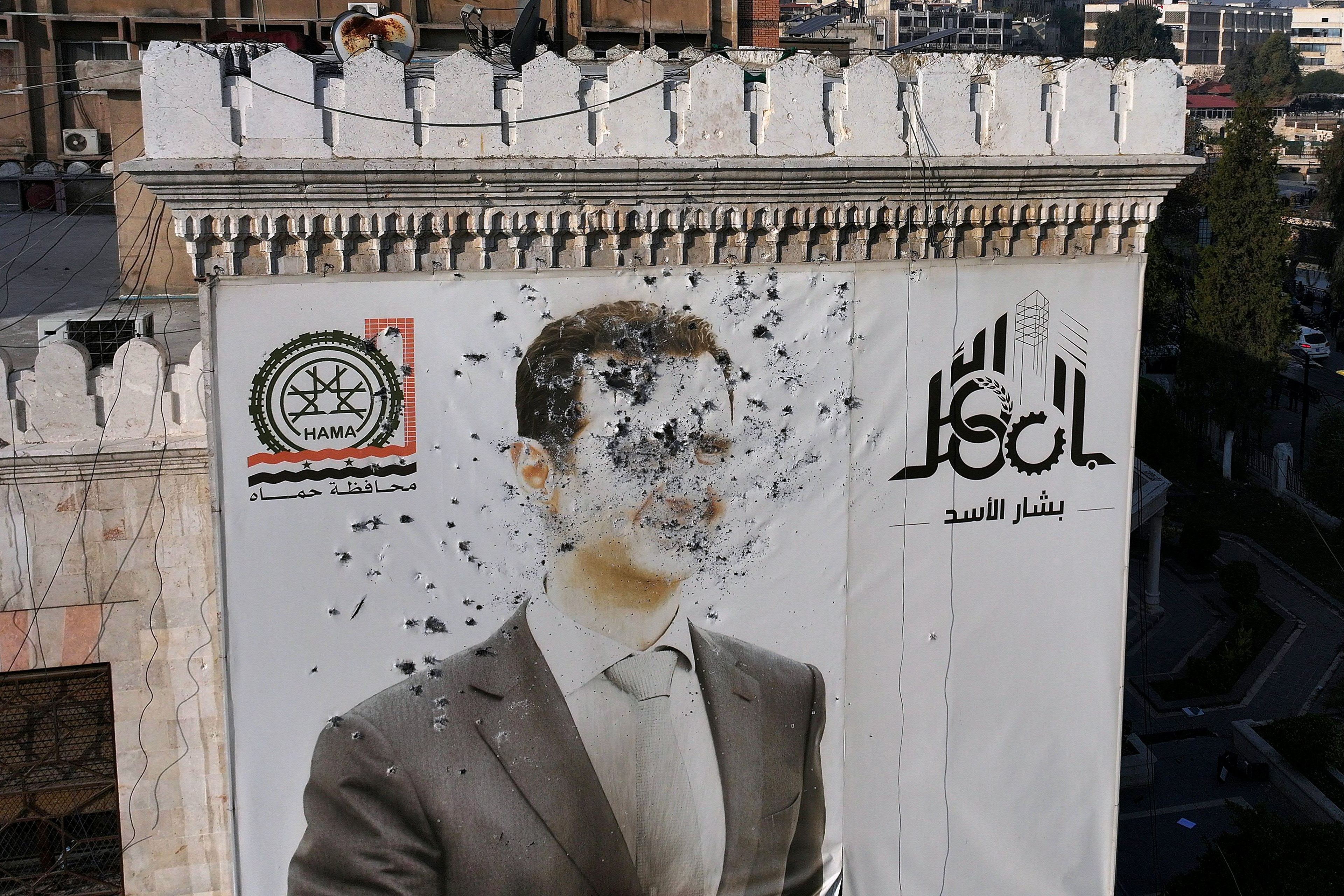This aerial picture shows a bullet-riddled portrait of Syrian President Bashar al-Assad adorning Hama's municipality building after it was defaced following the capture of the city by anti government fighters, on December 6, 2024. - Rebel forces pressing a lightning offensive in Syria aim to overthrow President Bashar al-Assad's rule, their Islamist leader said in an interview published on December 6. In little over a week, the offensive has seen Syria's second city Aleppo and strategically located Hama fall from Assad's control for the first time since the civil war began in 2011. (Photo by Omar HAJ KADOUR / AFP)