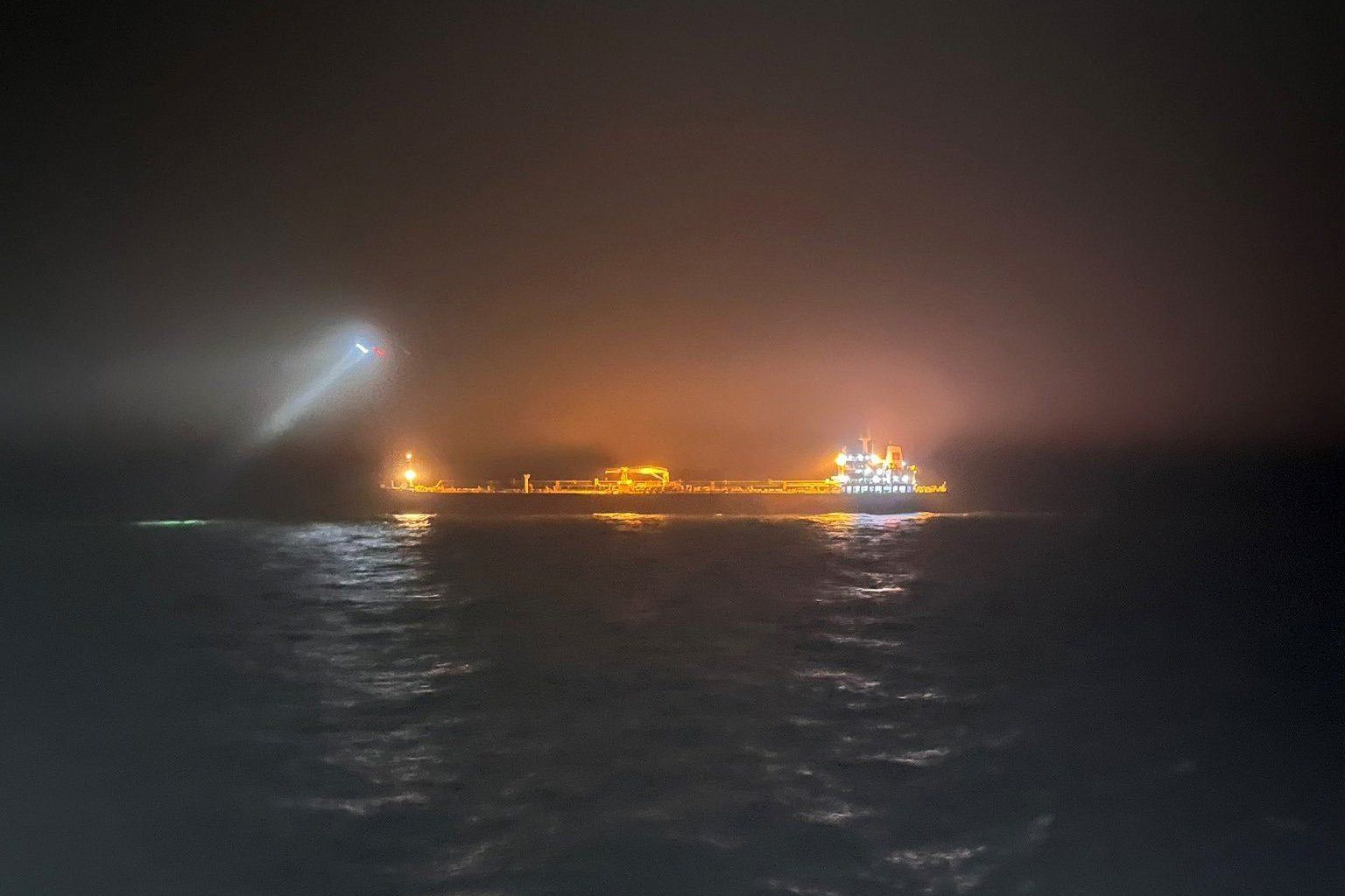 Nocne zdjęcie z oddali - widać oświetlony reflektorami statek na morzu