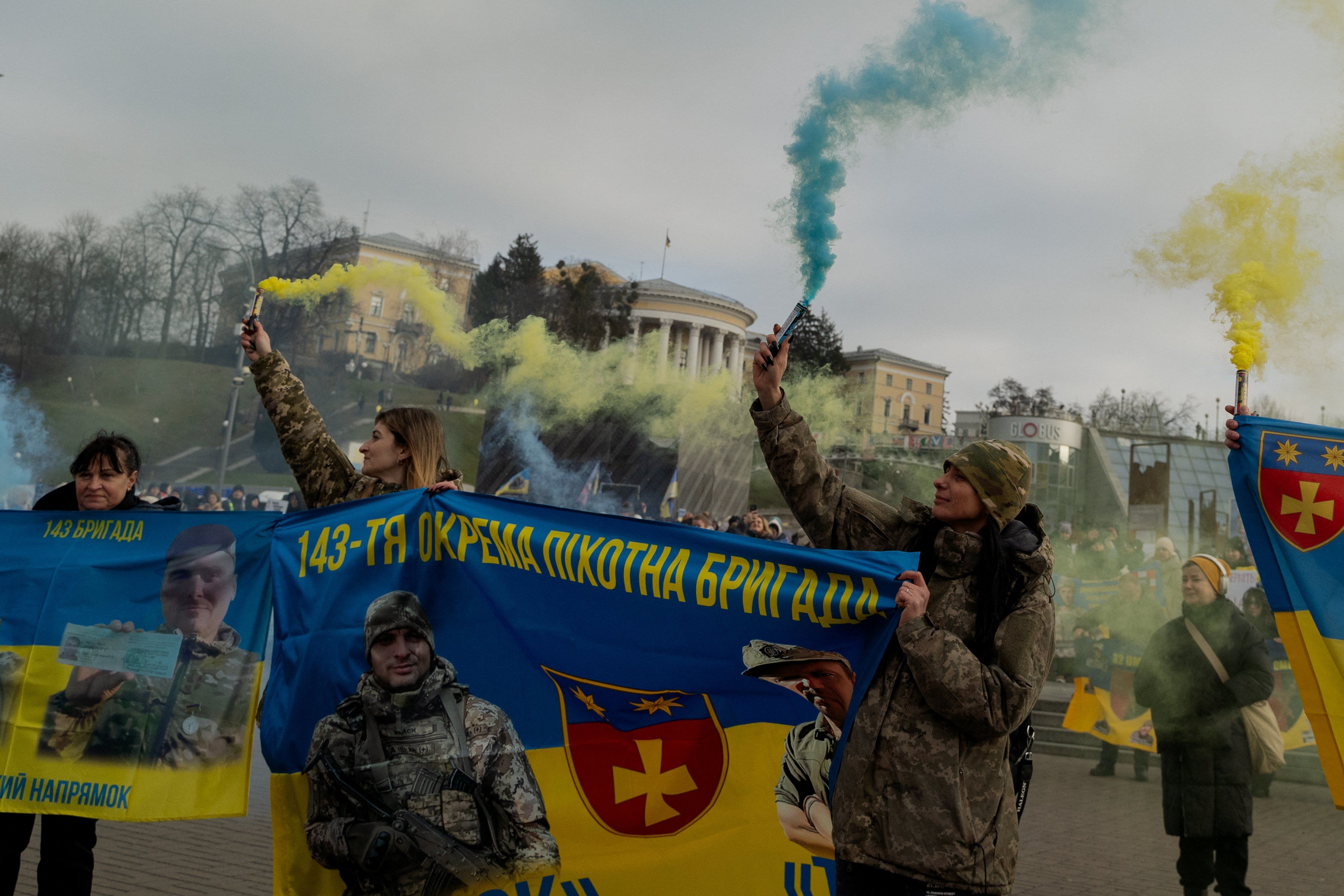 Protestujący ze sztandarem ukraińskiej brygady piechoty i niebieskimi oraz żółtymi flarami.