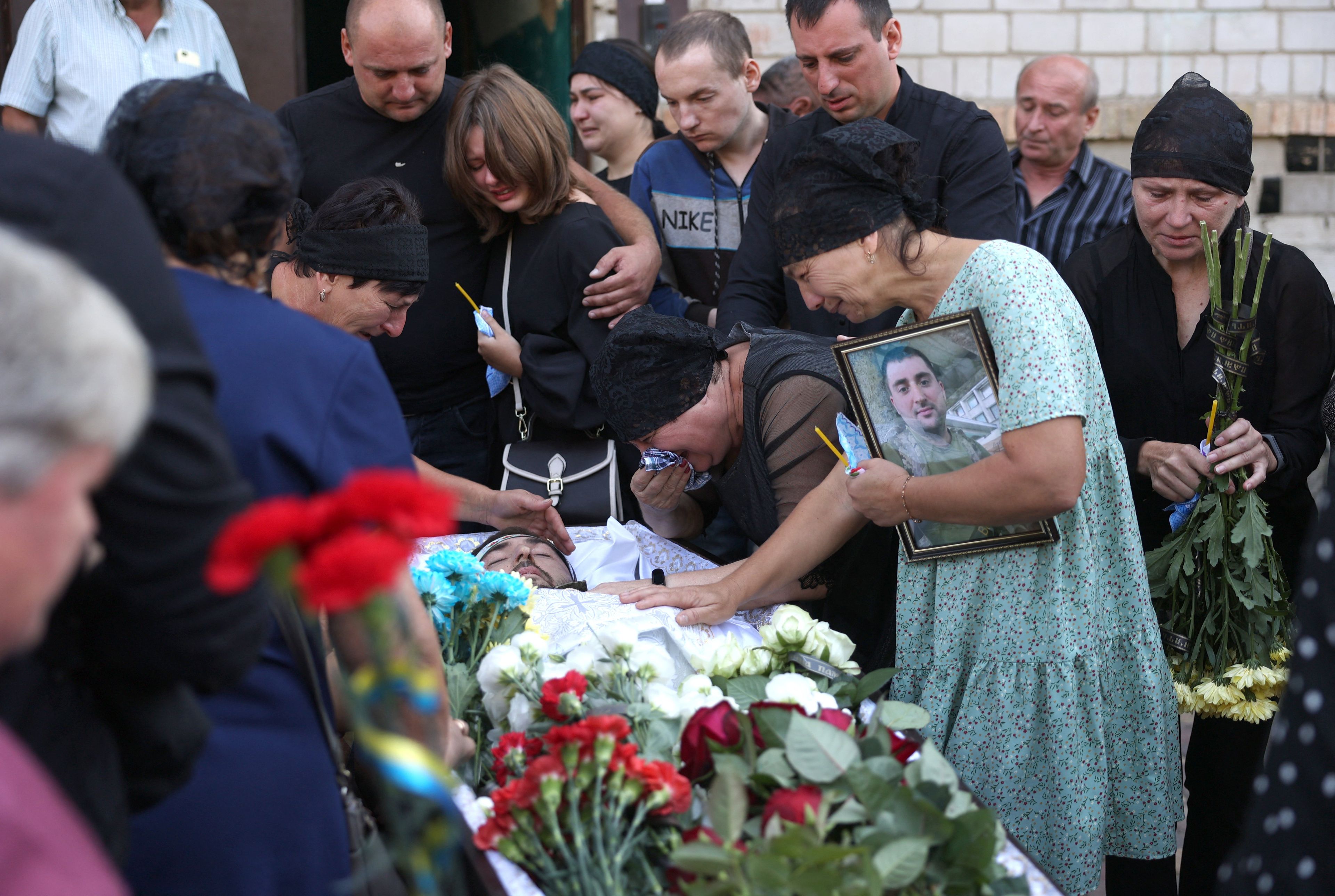 Rodzina żegna poległego żołnierza, ludzie płaczą nad trumną, przy niej widać kwiaty