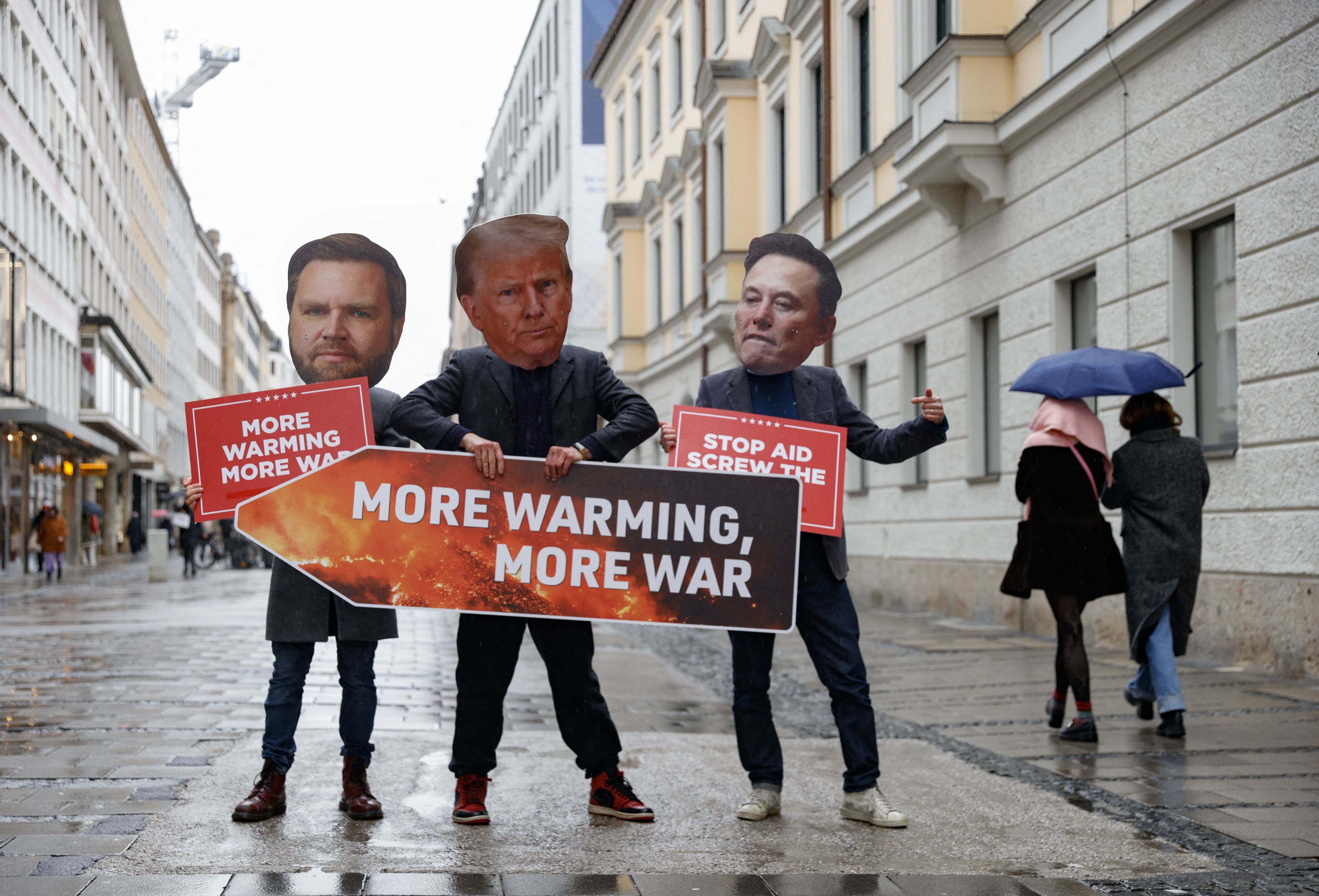 trzy osoby z maskami Trumpa, Vancea i Muska, trzymają napisa more warming more war