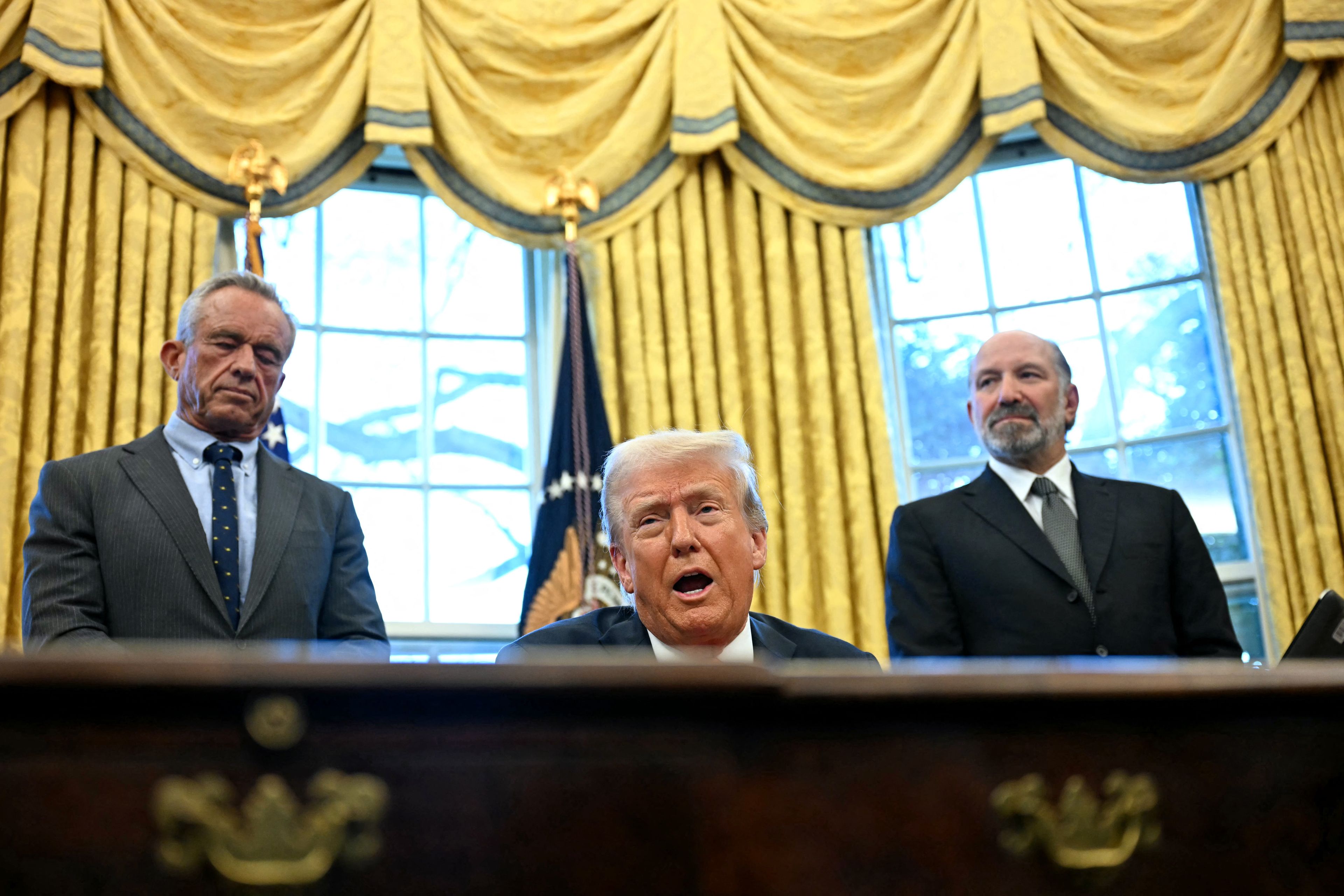 Donald Trump przemawia za biurkiem w Gabinecie Owalnym, w tle złote zasłony