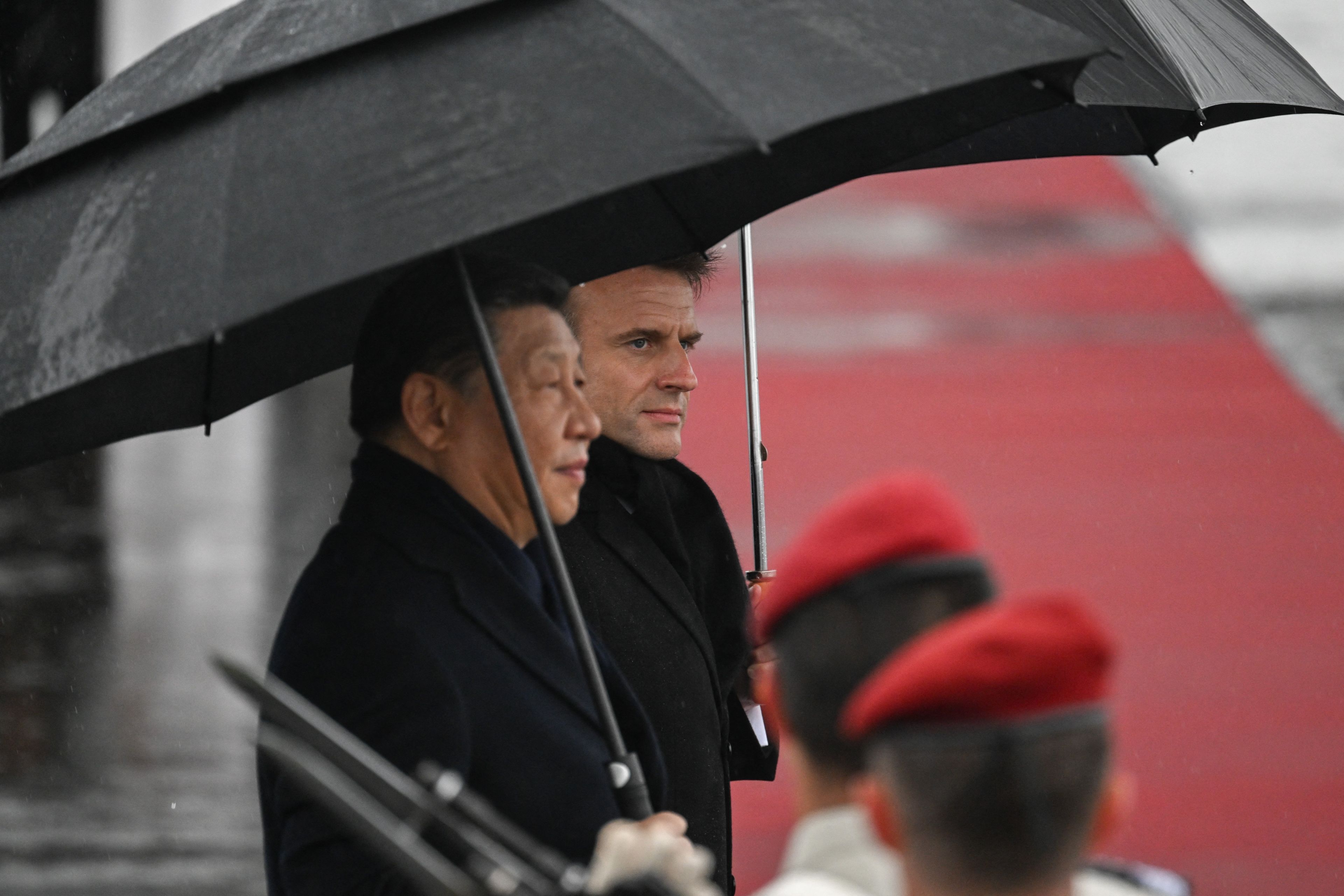 Przywódca Chin Xi Jinping i prezydent Francji Emmanuel Macron stoją pod czarnymi parasolami