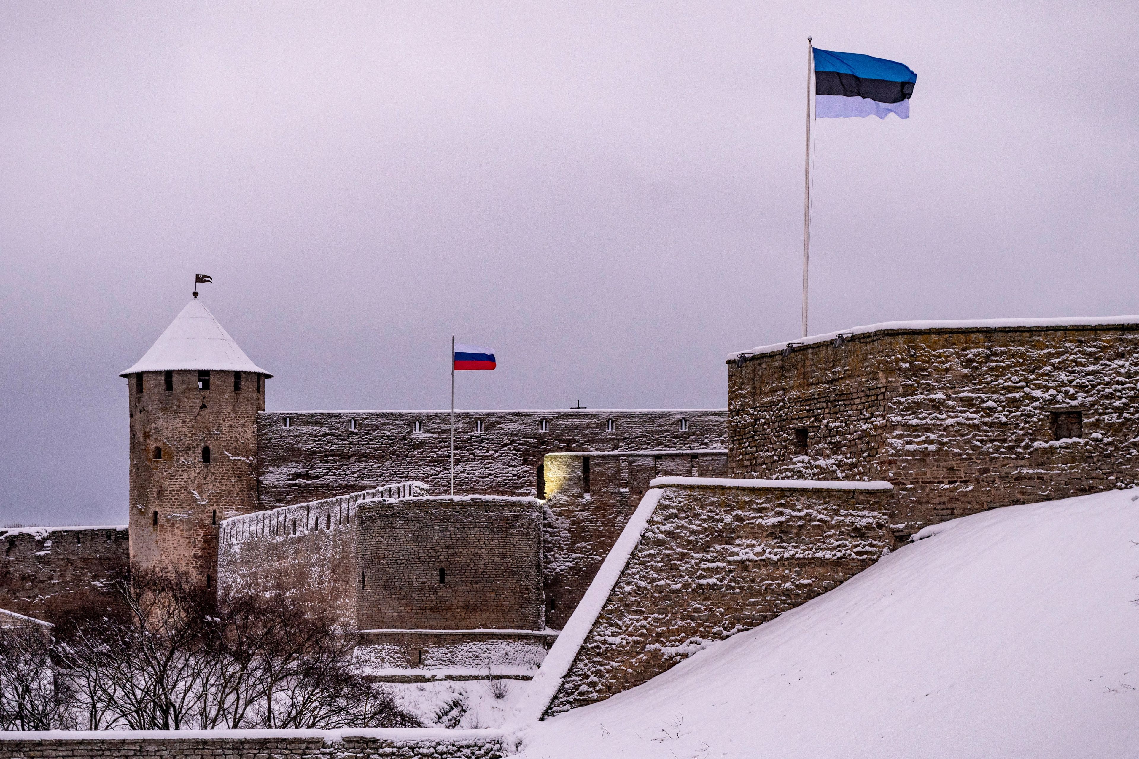 Ośnieżony zamek w Narwie na granicy rosyjsko-estońskiej, w dali powiewa flaga rosyjska, bliżej widać estońską