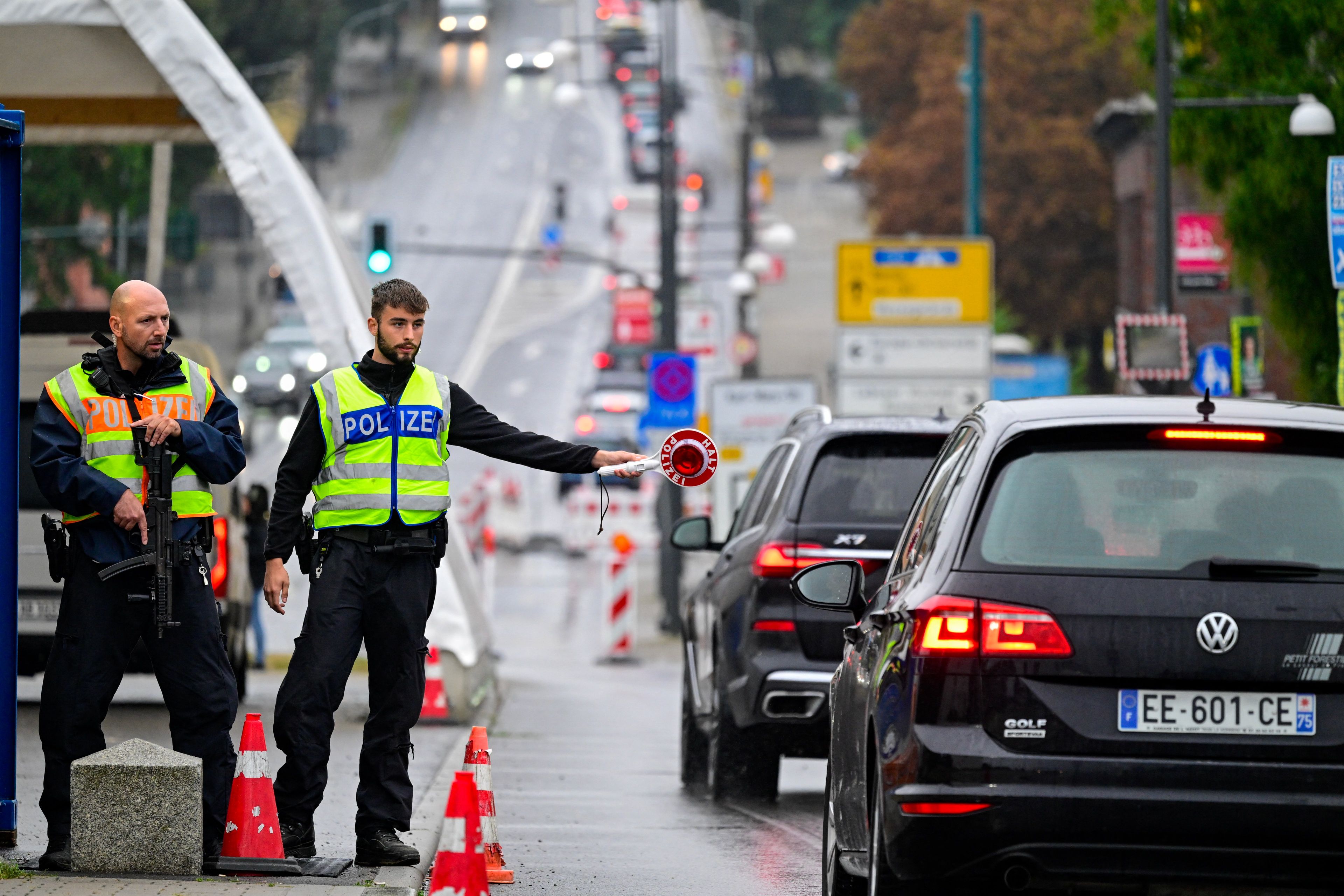 Niemiecki policjant ze znakiem stop w ręku zatrzymuje samochód