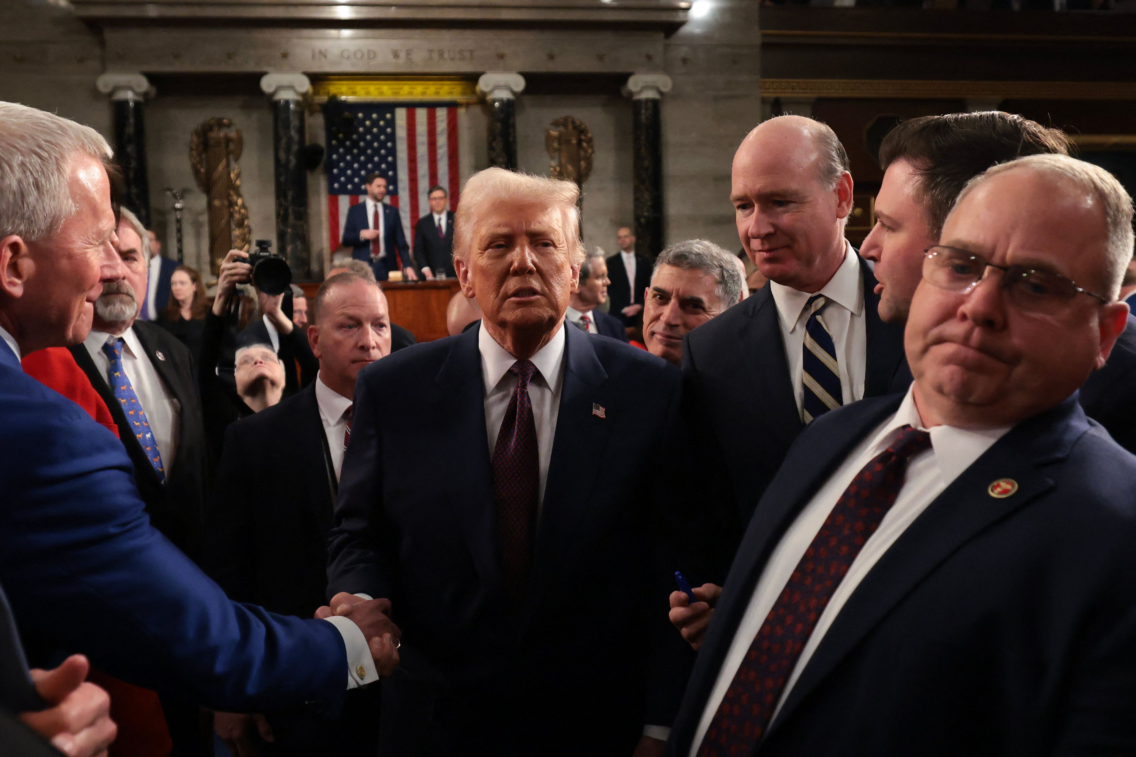 Donald Trump po przemówieniu w Kongresie ściska ręce słuchaczon. W tle mównica i flaga amerykańska