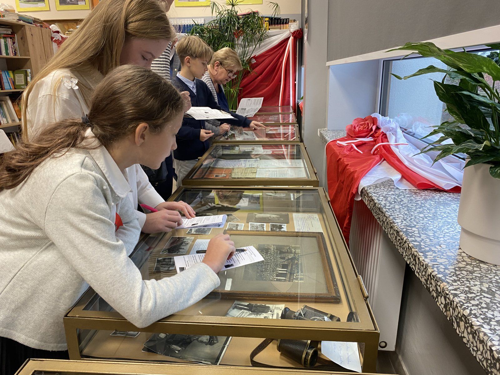 Dwie dziewczynki pochylają sie nad gablotą w bibliotece i rozwiązują zadanie