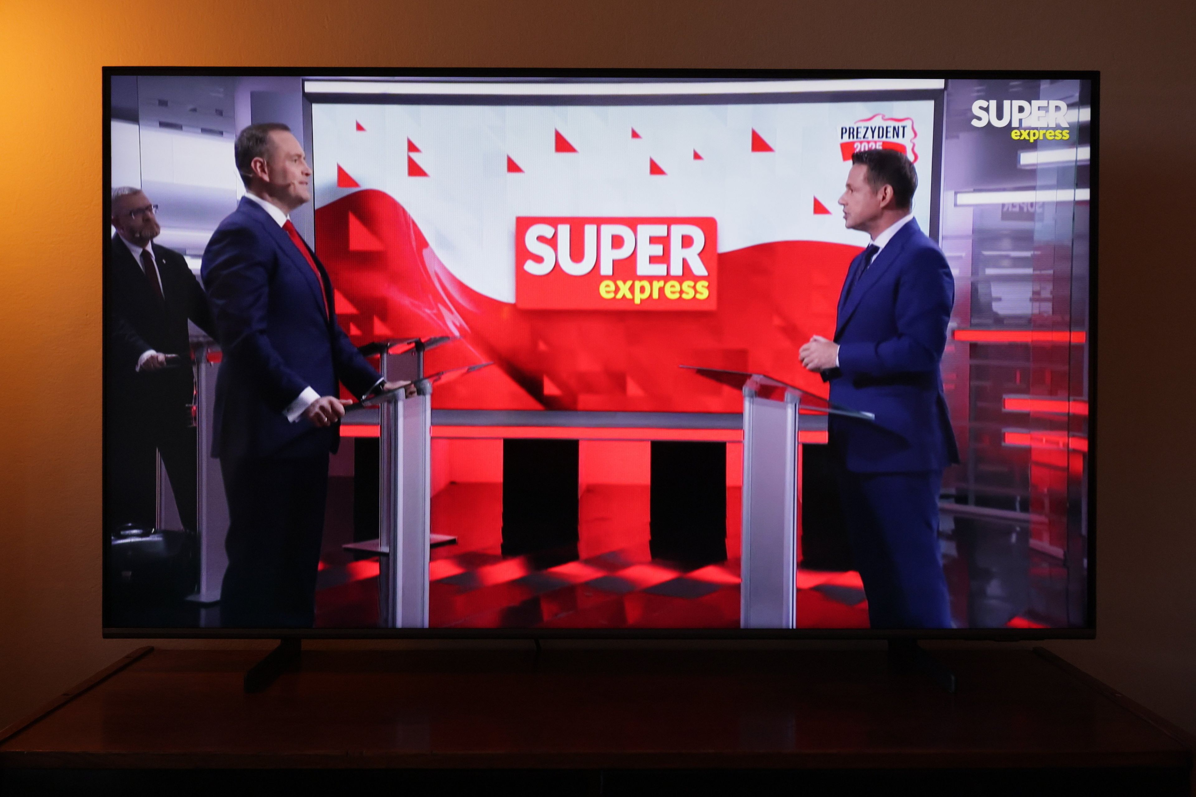 Dwaj mężczyźni stoją naprzeciw siebie. W tle napis Super Express