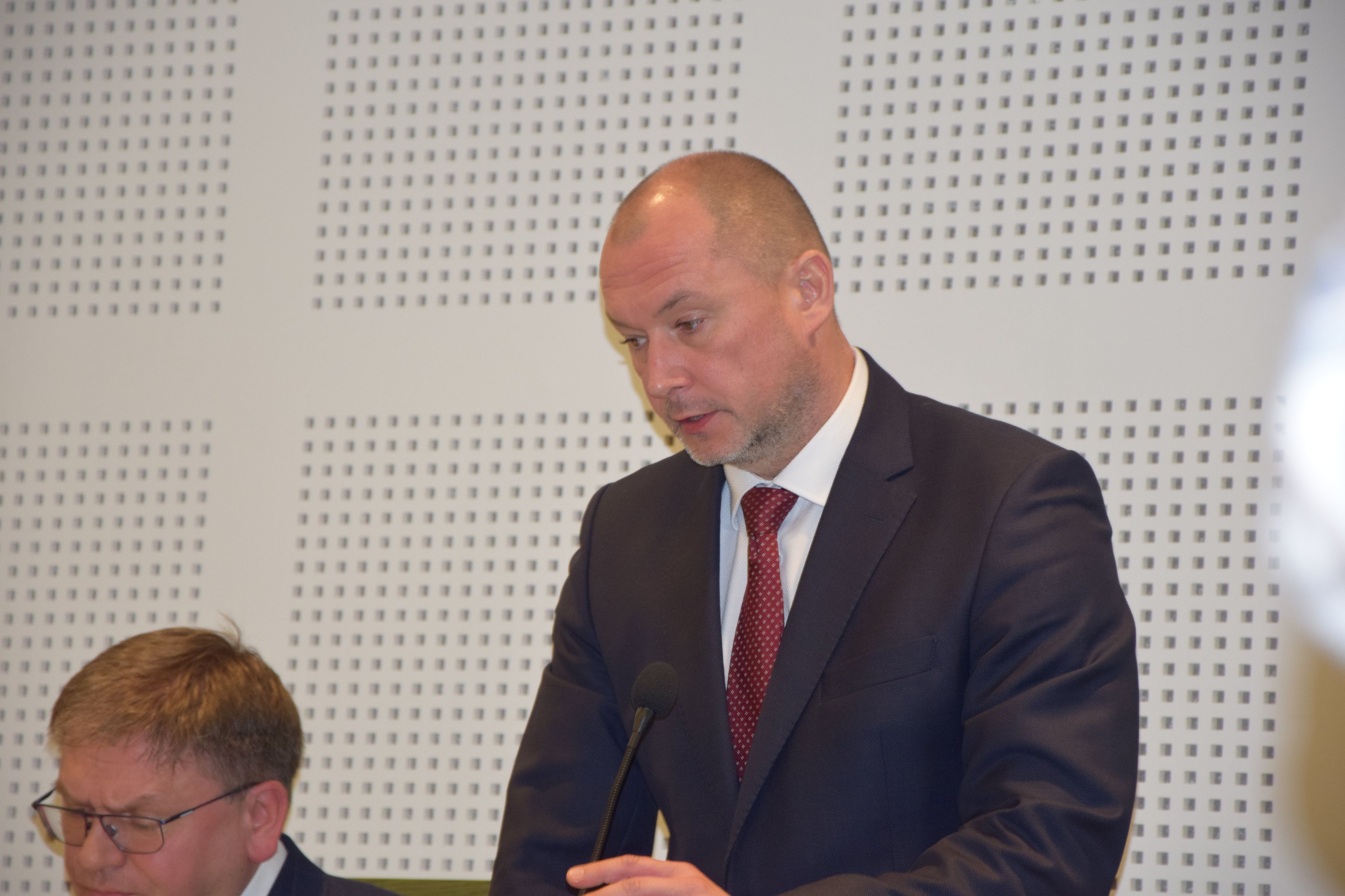 Mężczyzna w garniturze, białej koszuli i krawacie, stoi