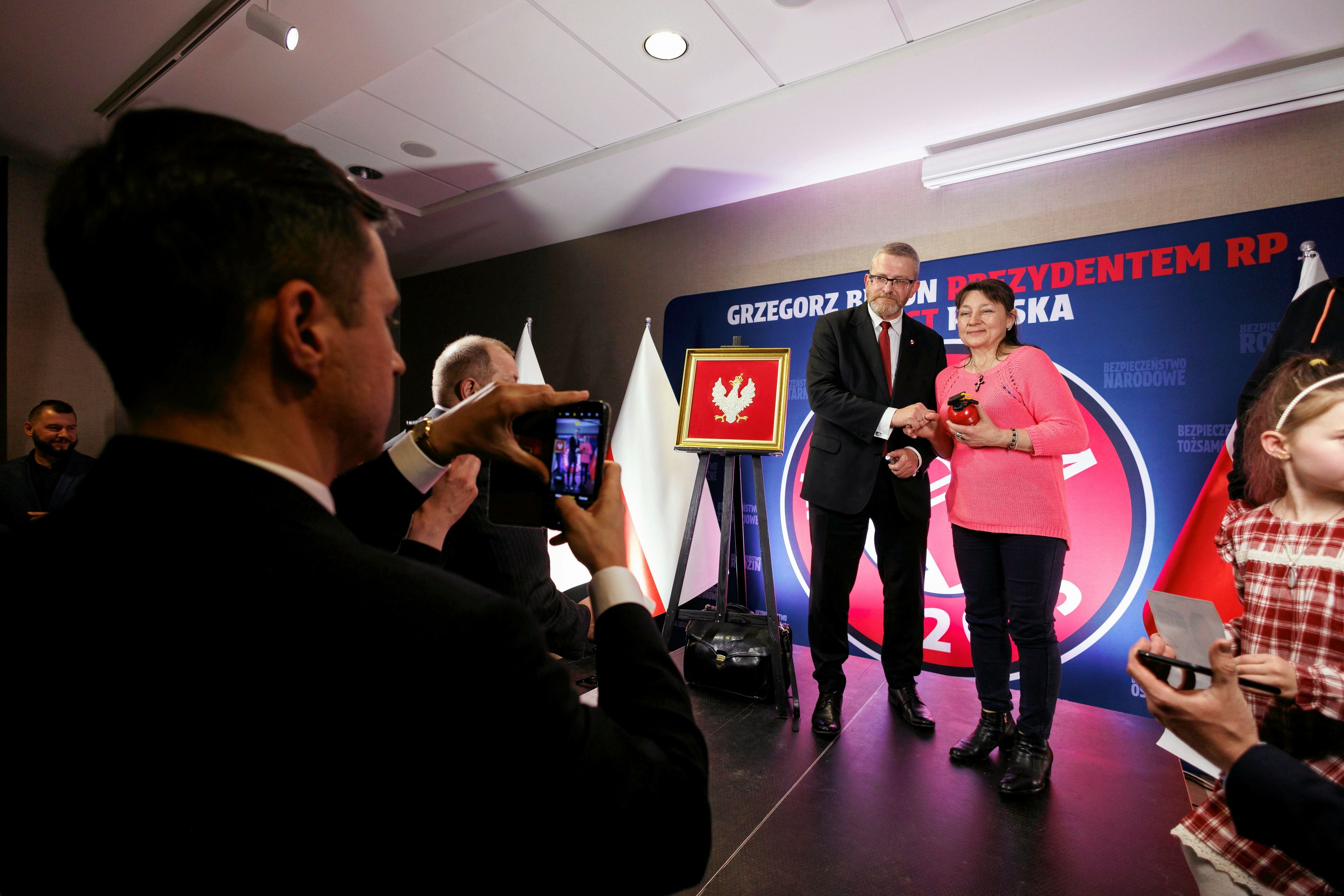 Mężczyzna i kobieta na podium, w tle napisa na banerze "Grzegorz Braun prezydentem Polski"
