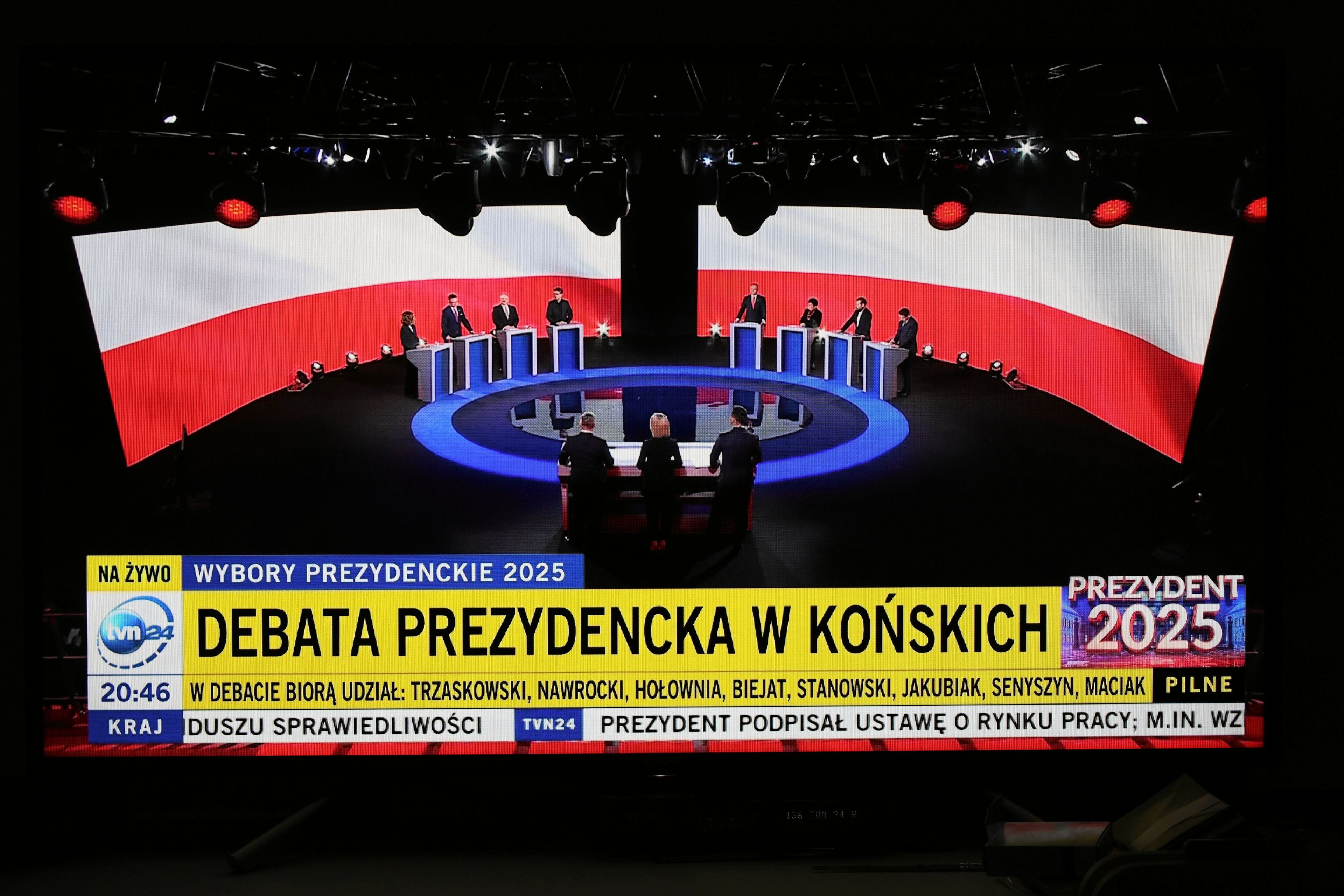 Widok sali w Końskich, filmowany z dużej odległości, na scenie w półkręgu podesty a za nimi kandydaci.