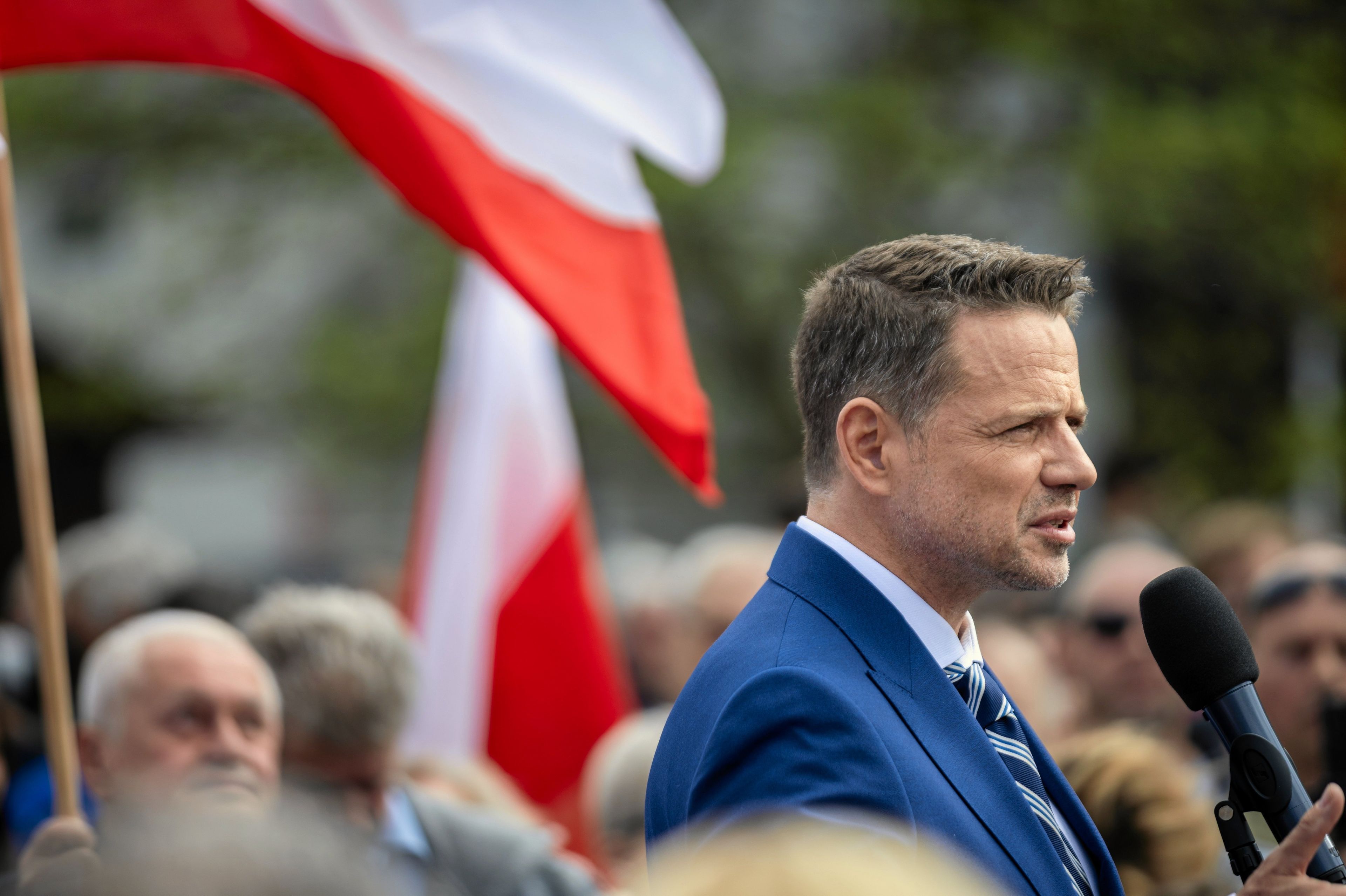 Mężczyzna stoi na podwyższeniu, wopkół tłum i białoczerwone flagi
