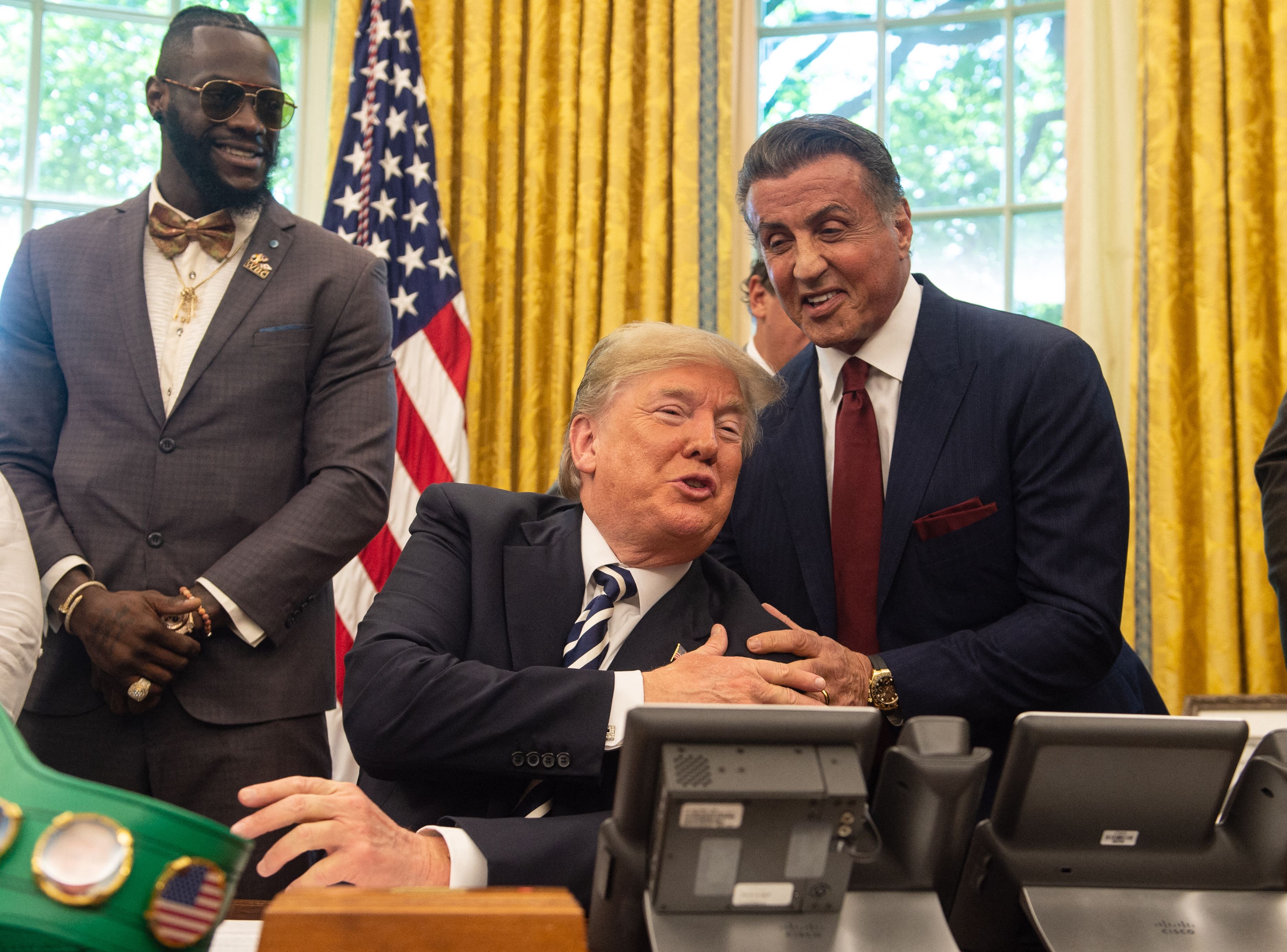 Donald Trump w towarzystwie ściskającego go Sylvestra Stallone i stojącego z boku boksera Lenoksa Lewisa w Gabinecie Owalnym
