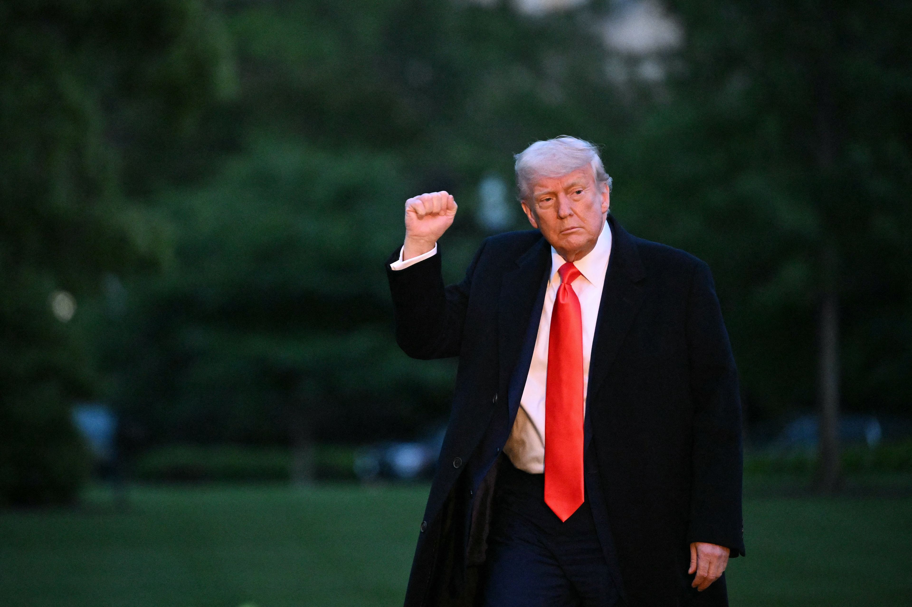 Donald Trump z uniesioną dłonią i długim czerwonym krawatem