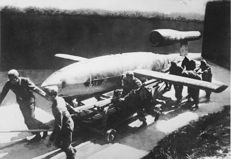 V1 vor dem Start
Aus guter Deckung wird "V1" an die Abschußstelle gerollt. Der Start erfolgt durch eine Pressluftanlage. Mit Hilfe eines Fernlenkverfahrens trifft die "V1" das befohlene Ziel. Die gleichbleibend hohe Geschwindigkeit, die von keinem Feindjäger erreicht wird, erhält "V1" von einem Raketenantrieb. Diese erste deutsche Vergeltungswaffe ist eine hervorragende Schöpfung unserer Luftrüstung.