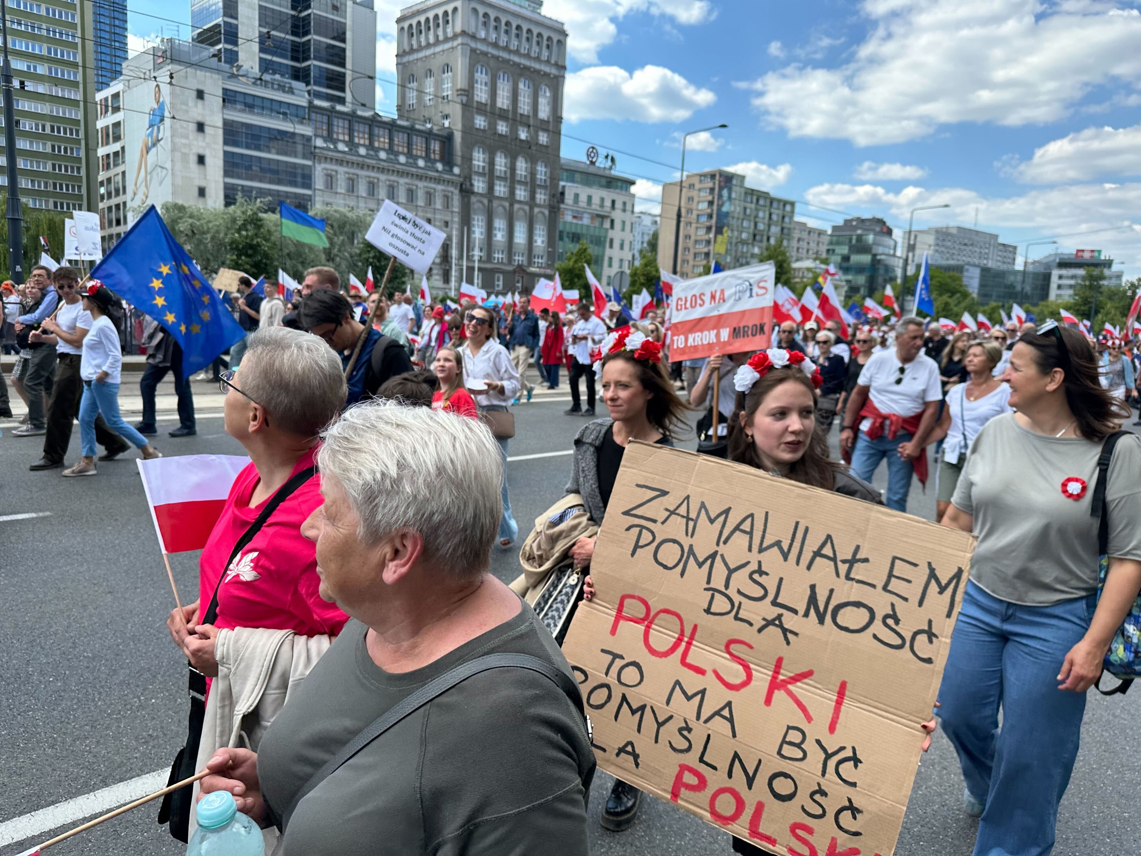 Tłum ludzi idzie ulicą, jedna z osób trzyma transparent z napisem "Zamawiałam pomyślność dla Polski, to ma być pomyślność dla Polski"
