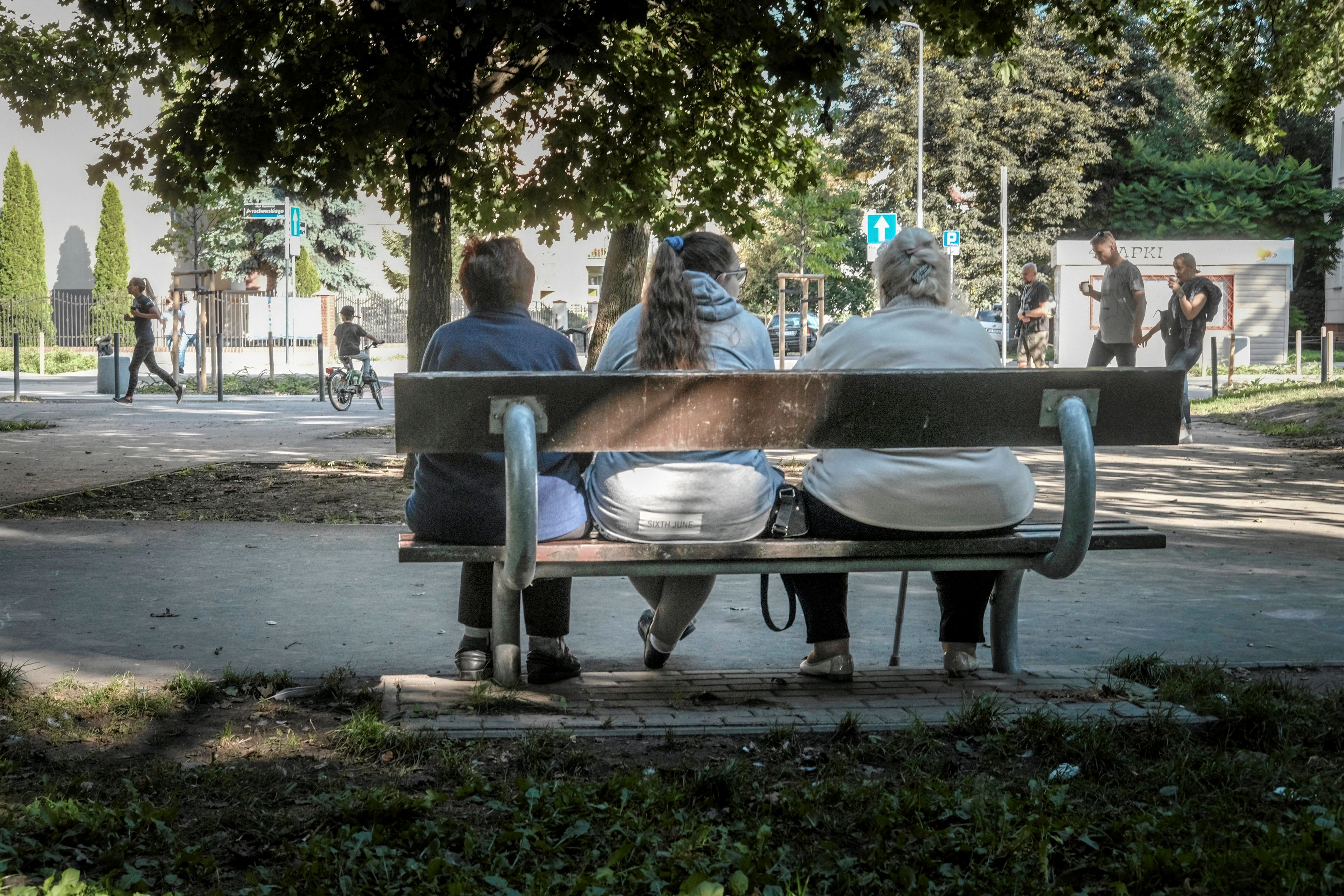 Trzy kobiety z nadwagą siedzą na ławce, widziane z tyłu