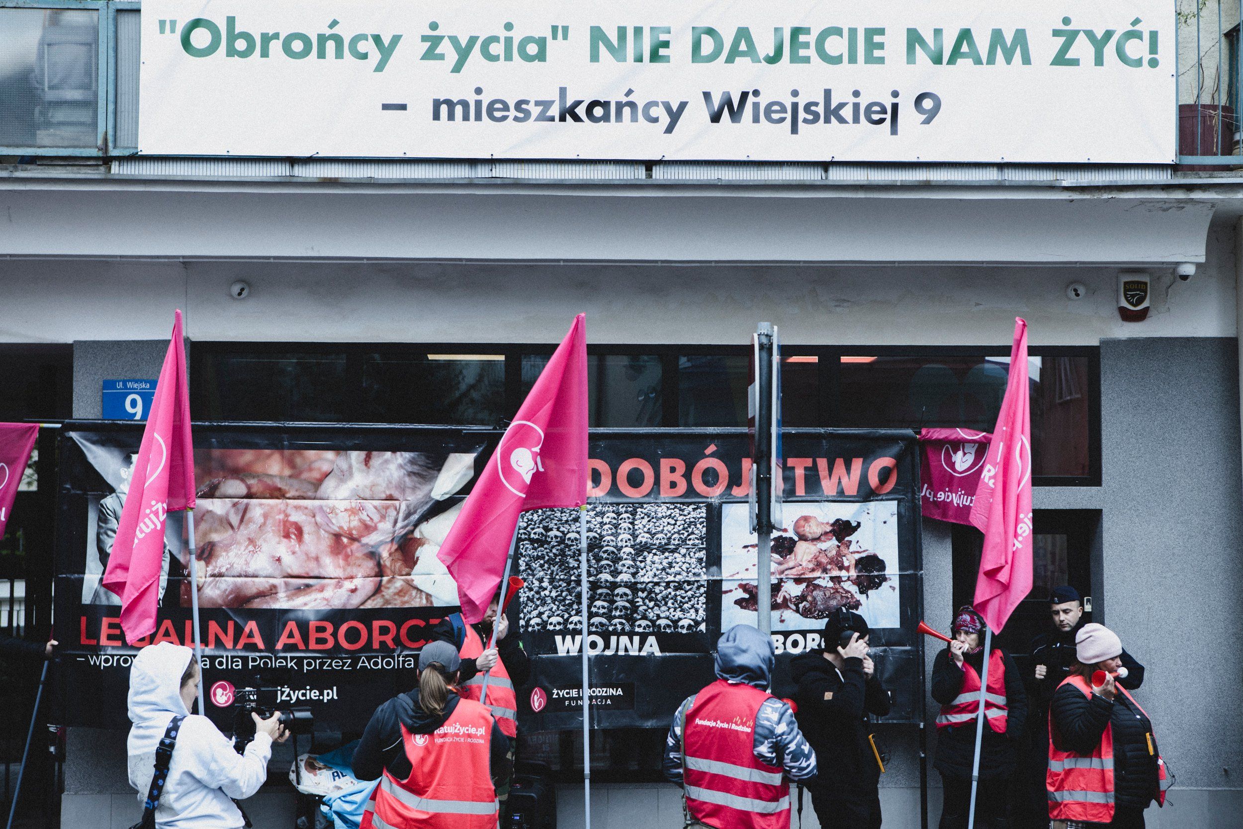 Kolejny raz pod przychodnią Abotak przeciwnicy aborcji zorganizowali swoje zgromadzenie. Przez wiele godzin uzbrojeni w wuwuzele, głośne nagranie płaczu dziecka utrudniają pracę przychodni, życie mieszkańców oraz zwykłe przejście przez chodnik przypadkowym przechodniom.
Dzisiaj kilka razy doszło do agresji słownej i naruszania nietykalności cielesnej, zwłaszcza ze strony jednej uczestniczki zgromadzenia, w stosunku do przechodniów oraz osób dokumentujących całe zajście. Byliśmy wulgarnie wyzywani, wypychani i kopani, w tym ja, co finalnie będzie skutkowało zgłoszeniem tego na policji.
Przeciwnicy aborcji regularnie trąbią prosto w ucho osobom, które chcą wejść do przychodni. Co ciekawe sami noszą słuchawki chroniące przed hałasem.
Osoby pracujące w Abotak dostały dzisiaj wsparcie miedzy innymi  od Polskie Babcie, Strajk Kobiet, Wschód oraz przyjaciół i przyjaciółek, które stały z transparentami i plakatami po drugiej stronie ulicy lub bezpośrednio pod drzwiami przychodni.